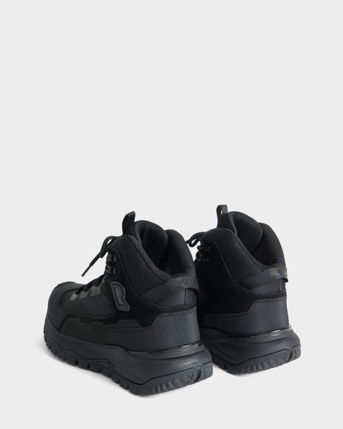 A pair of REXON - 6226503 Black high-top sneakers by Rudsak are positioned on a light gray background, angled slightly away to highlight the backs and outer sides of each shoe.