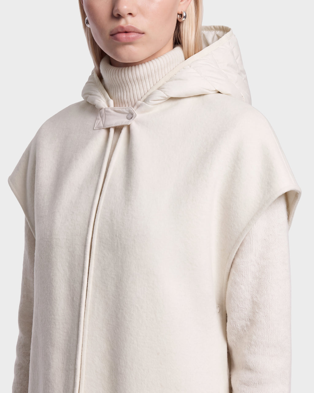 A person wearing the ROXANE - 8526677 Vanilla hooded cape by Rudsak over a cream turtleneck sweater, featuring short sleeves and a single button at the neck. Only the lower half of their face is visible.