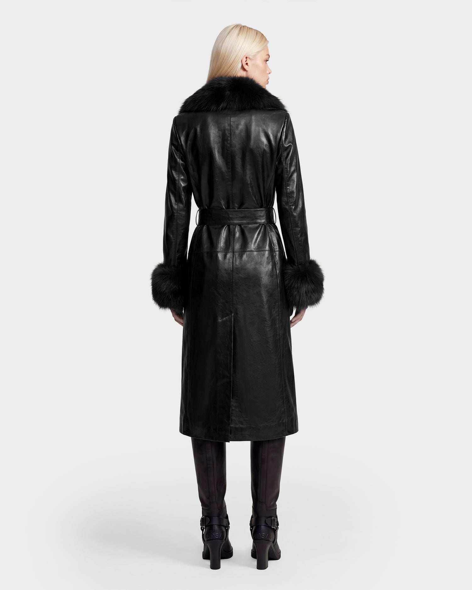 A person with long blond hair wears the VIVIANNE - 8126933 Black leather coat by Rudsak, featuring a fur collar and cuffs, paired with black pants and boots, standing with their back to the camera against a plain light background—perfect inspiration for your next look. Available for pre-order now from Rudsak, with expected delivery in August 2026.