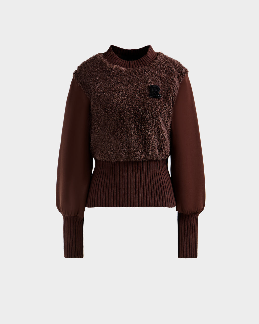 The FLORENCE - 8525546 Mocha by Rudsak is a brown women's long-sleeve faux fur top with a textured fuzzy front, ribbed cuffs and waistband, and a small black 'R' patch on the left chest. Set against a plain light gray background.