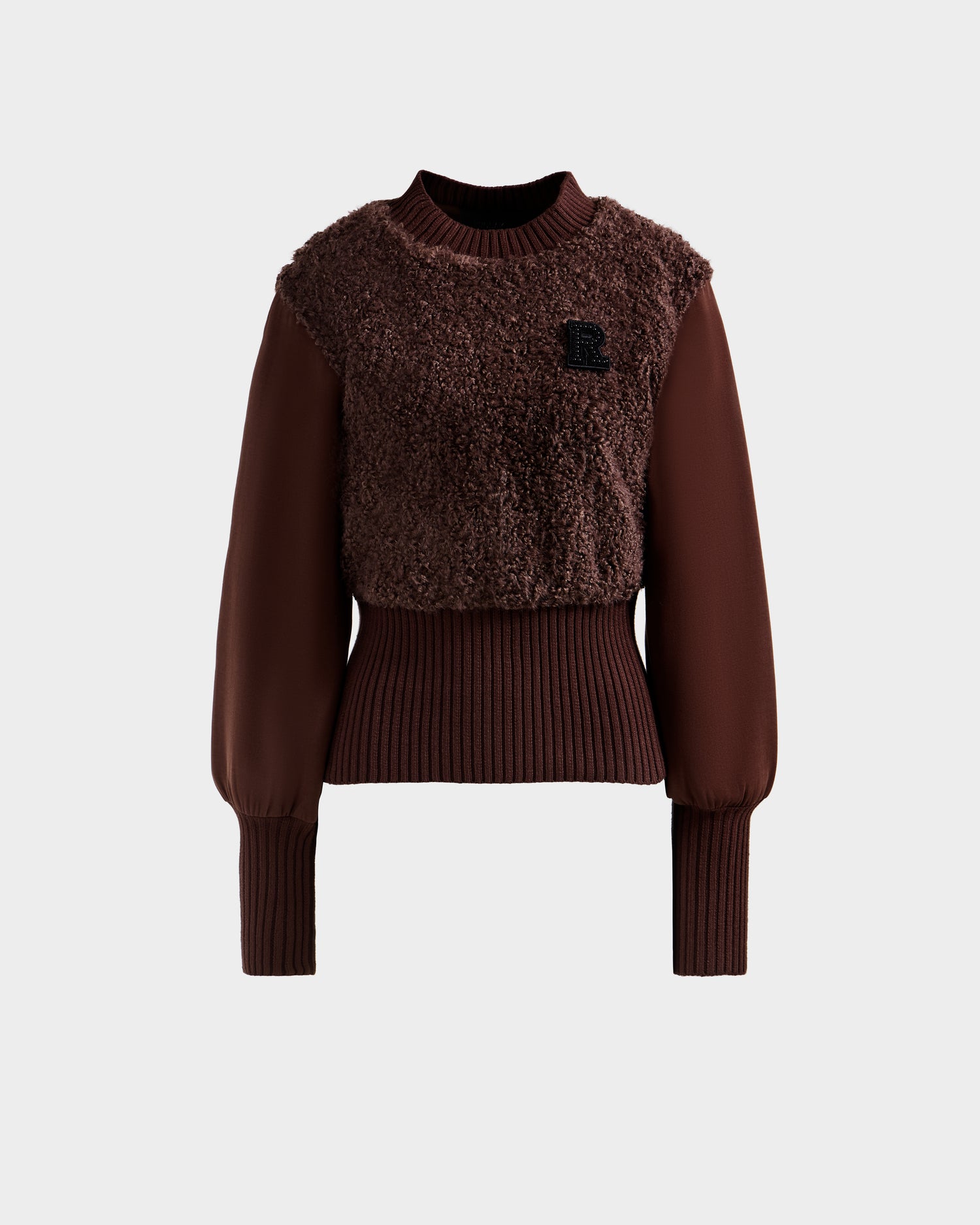 The FLORENCE - 8525546 Mocha by Rudsak is a brown women's long-sleeve faux fur top with a textured fuzzy front, ribbed cuffs and waistband, and a small black 'R' patch on the left chest. Set against a plain light gray background.