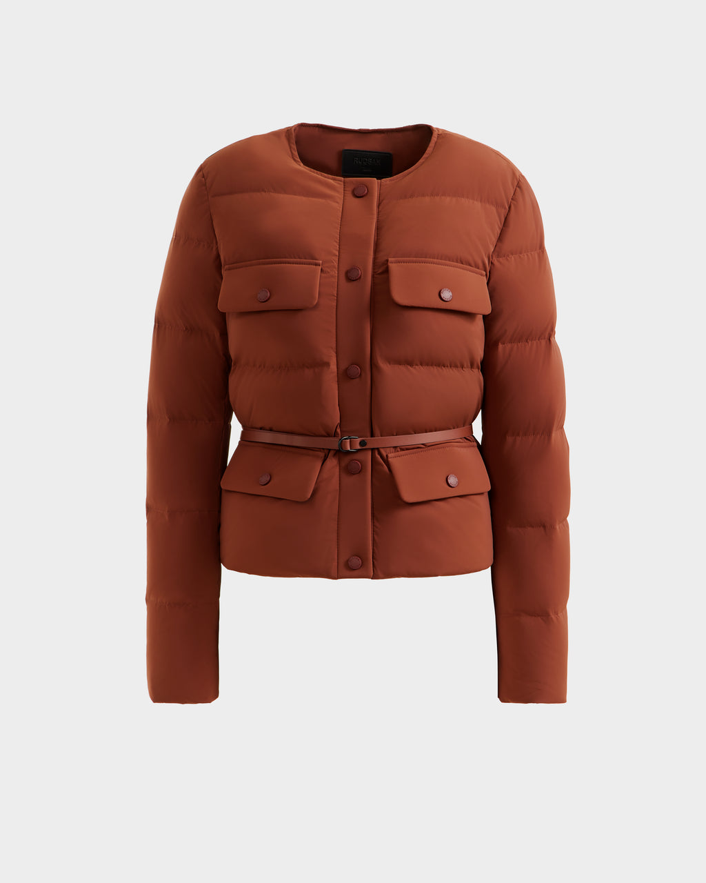 The Rudsak FRANCESCA - 8125021 Rust is a rust-colored, waist-length quilted puffer jacket with long sleeves, chest and lower flap pockets, a belted waist, and round neckline—lightweight outerwear shown on a plain white background.
