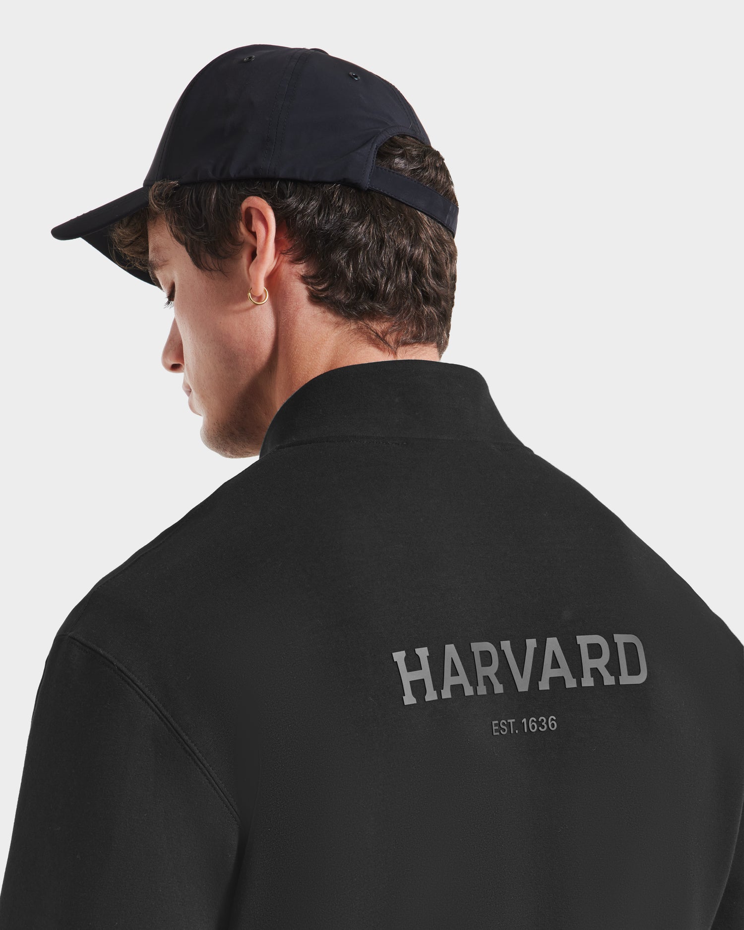 Someone wearing a black Rudsak FREMONT HV - H525501 pullover featuring HARVARD and EST. 1636 in white on the back, made from premium cotton blend, is seen from behind against a plain background.