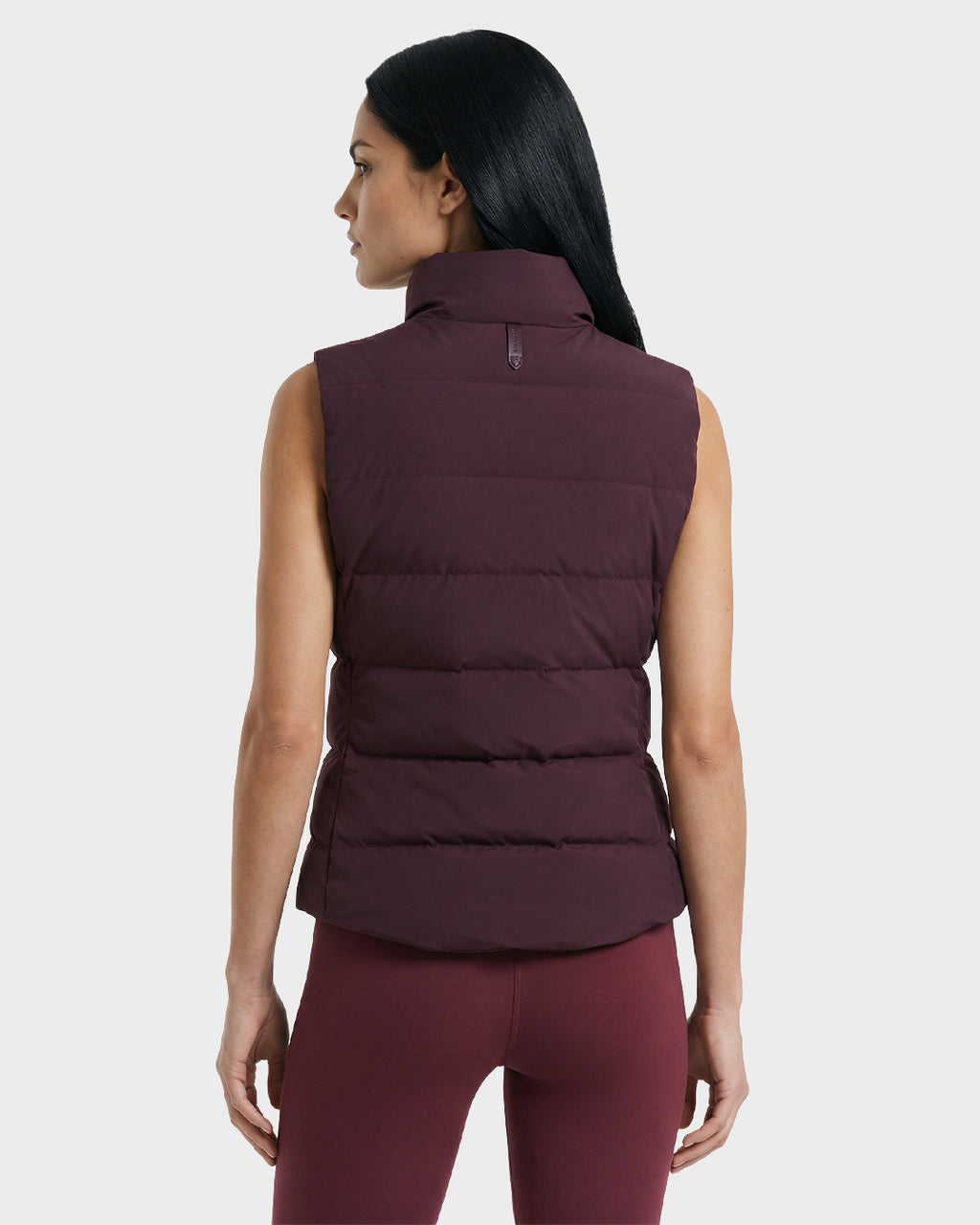 A woman with straight black hair wears the Rudsak GABRIELA - 8125014 Bordeaux puffer vest and matching leggings, standing against a plain light gray background with her head slightly turned to the side.