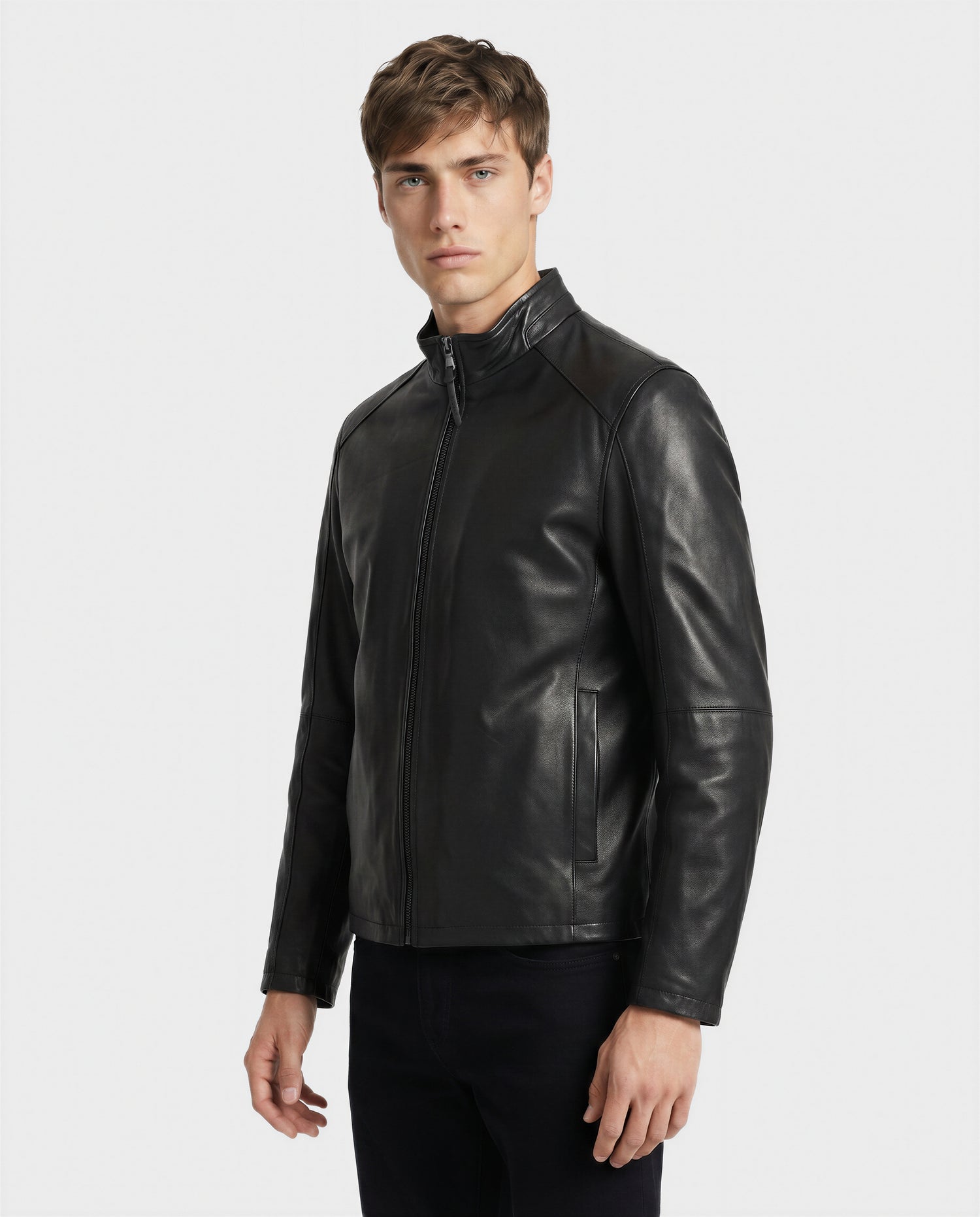 A young man with short brown hair wears the Rudsak GARY - M126061 Black leather jacket, featuring a stand collar and zip closure, paired with black pants against a plain white background.