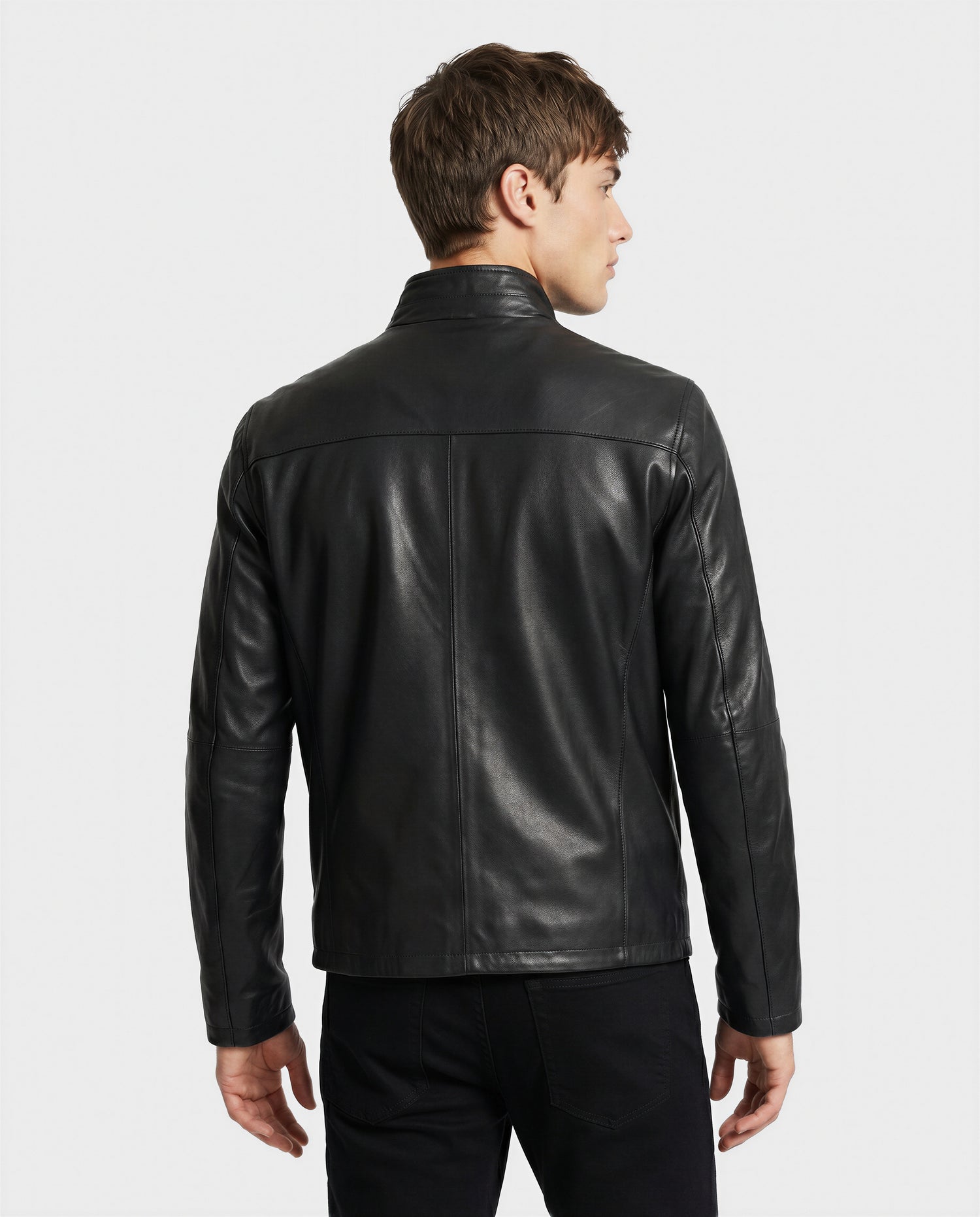 A man wearing the Rudsak GARY - M126061 Black leather jacket and black pants stands with his back to the camera, looking to his left against a light plain background.