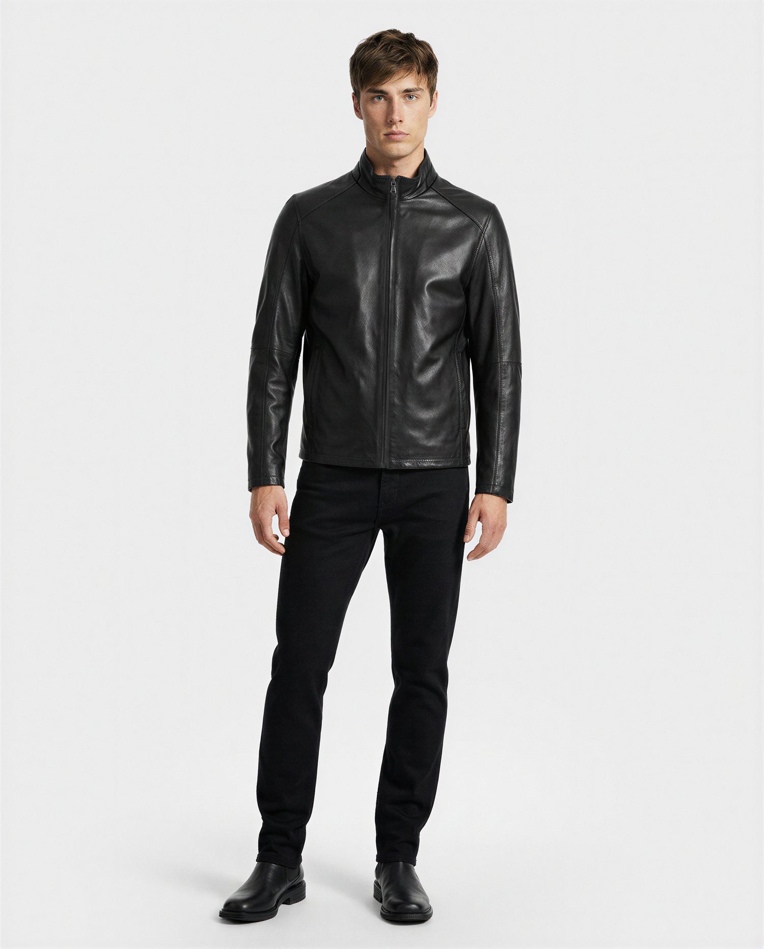A man stands facing forward against a plain white background, wearing the Rudsak GARY - M126061 Black leather jacket, paired with black pants and black boots.