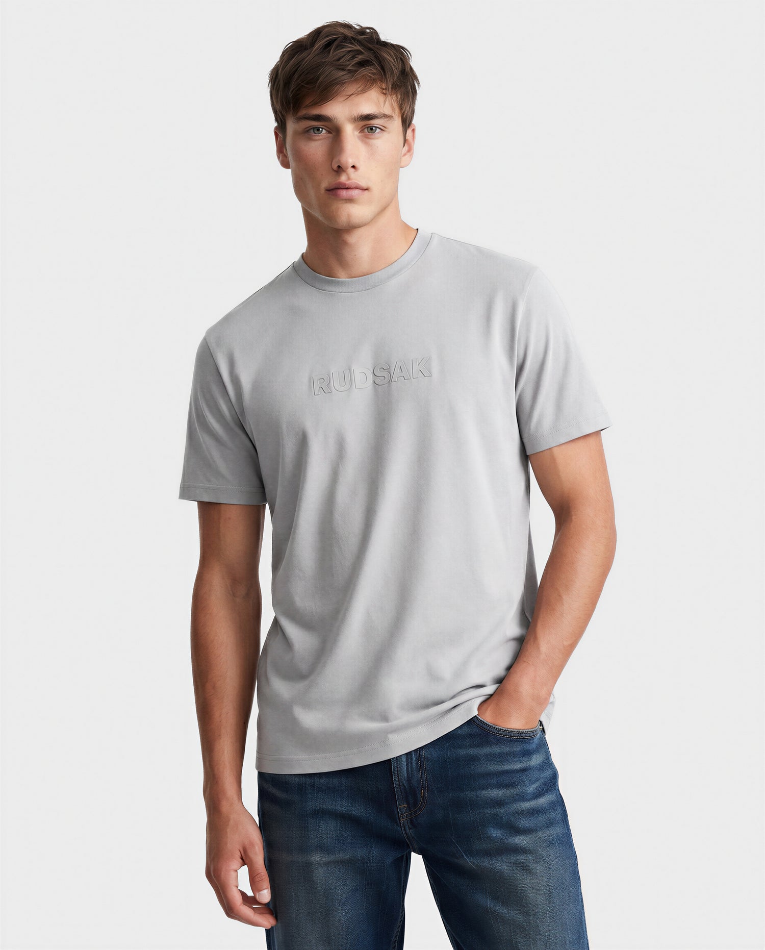 A young man with short brown hair wears the Rudsak FERDI - 6522005 Mushroom T-shirt and blue jeans, standing against a plain white background with one hand in his pocket.