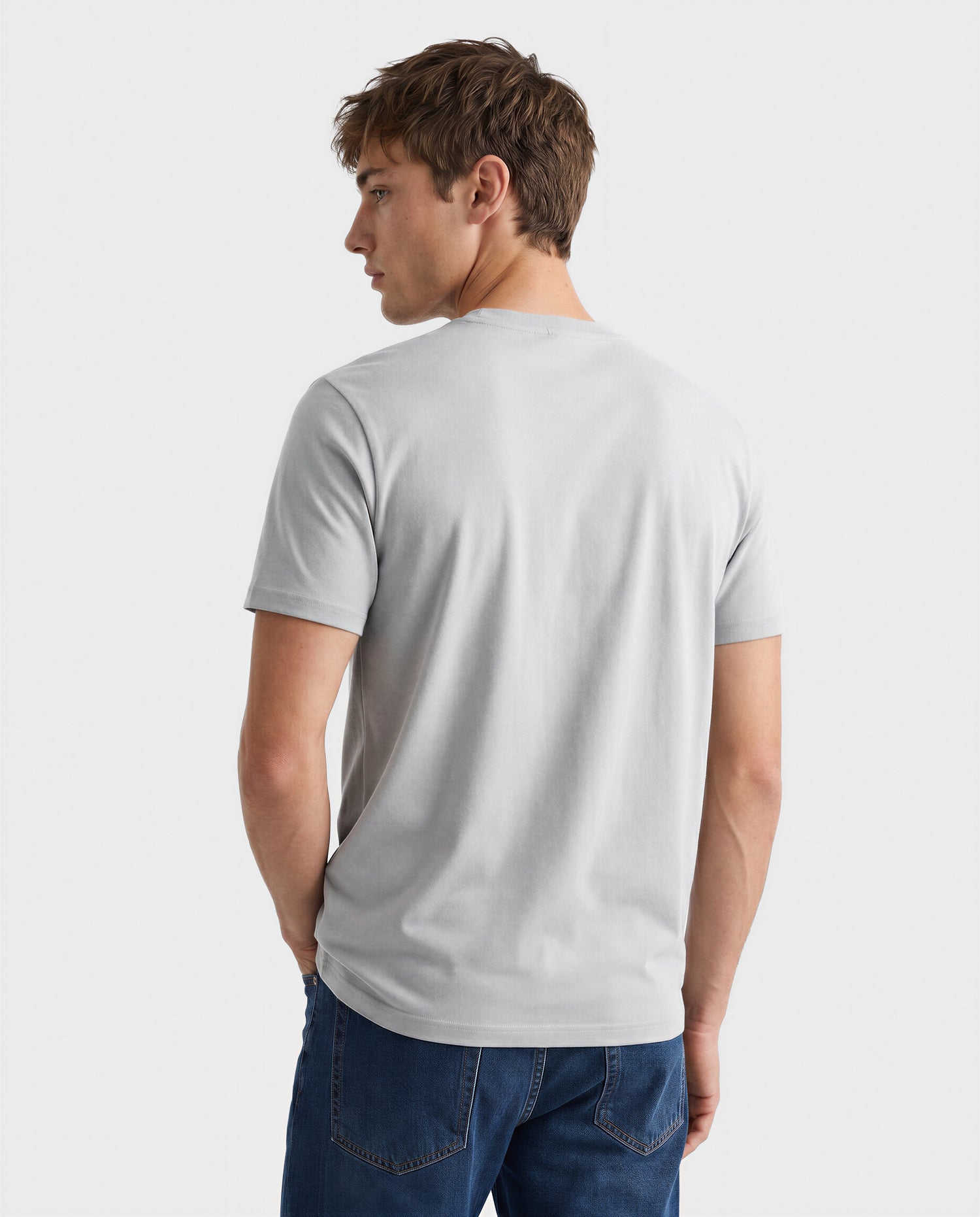 A man models the Rudsak FERDI - 6522005 Mushroom light gray short-sleeve t-shirt with blue jeans, standing against a white backdrop and looking over his left shoulder.