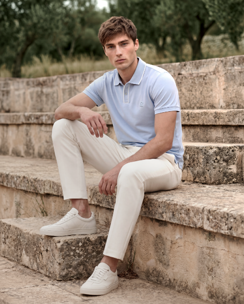 Man sitting on stone steps wearing a light blue polo shirt and white pants.