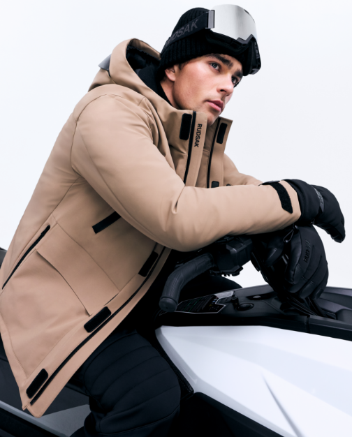 Person wearing a beige winter coat and black gloves sitting on a motorcycle with a white background