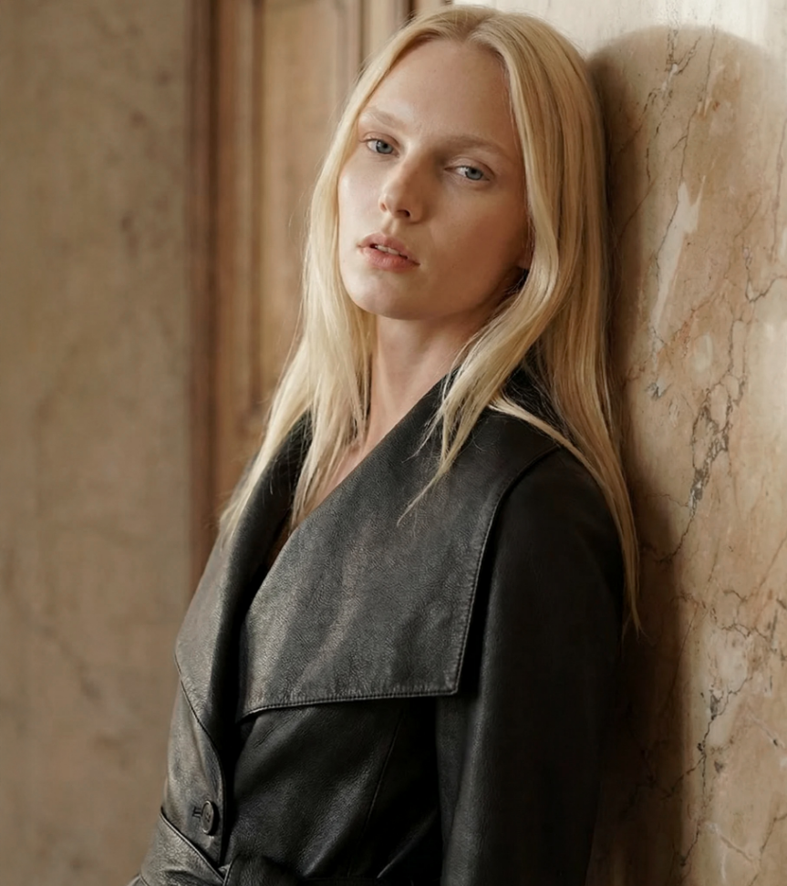 Woman with blonde hair leaning against a marble wall