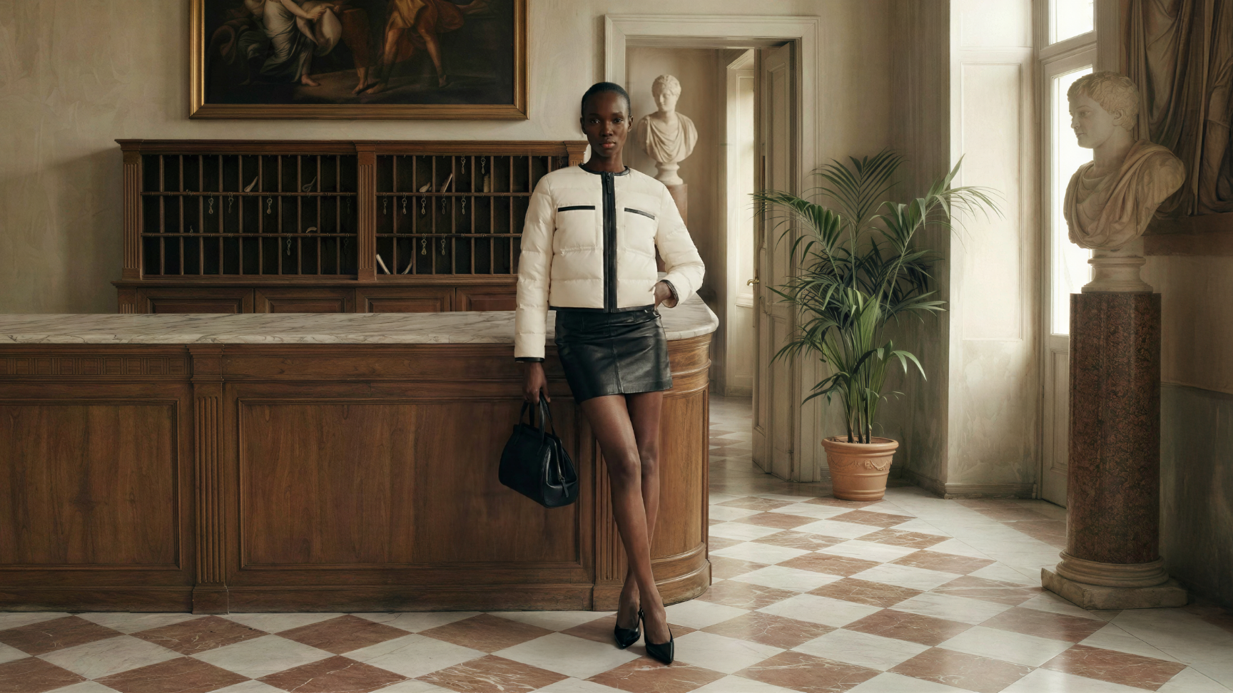 Woman in a stylish outfit standing in an elegant interior setting with classical sculptures and decor.