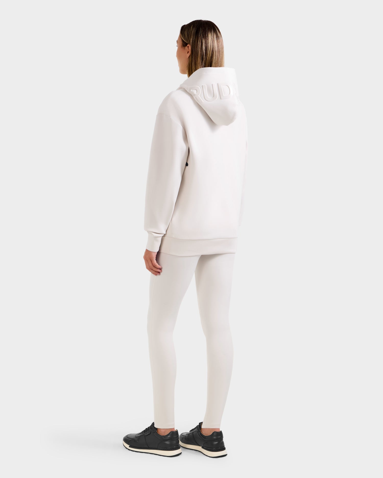 A person stands facing away, wearing the Rudsak LEROY - U525509 Iceland W off-white cotton-blend hoodie and matching leggings with black sneakers, set against a plain light background.