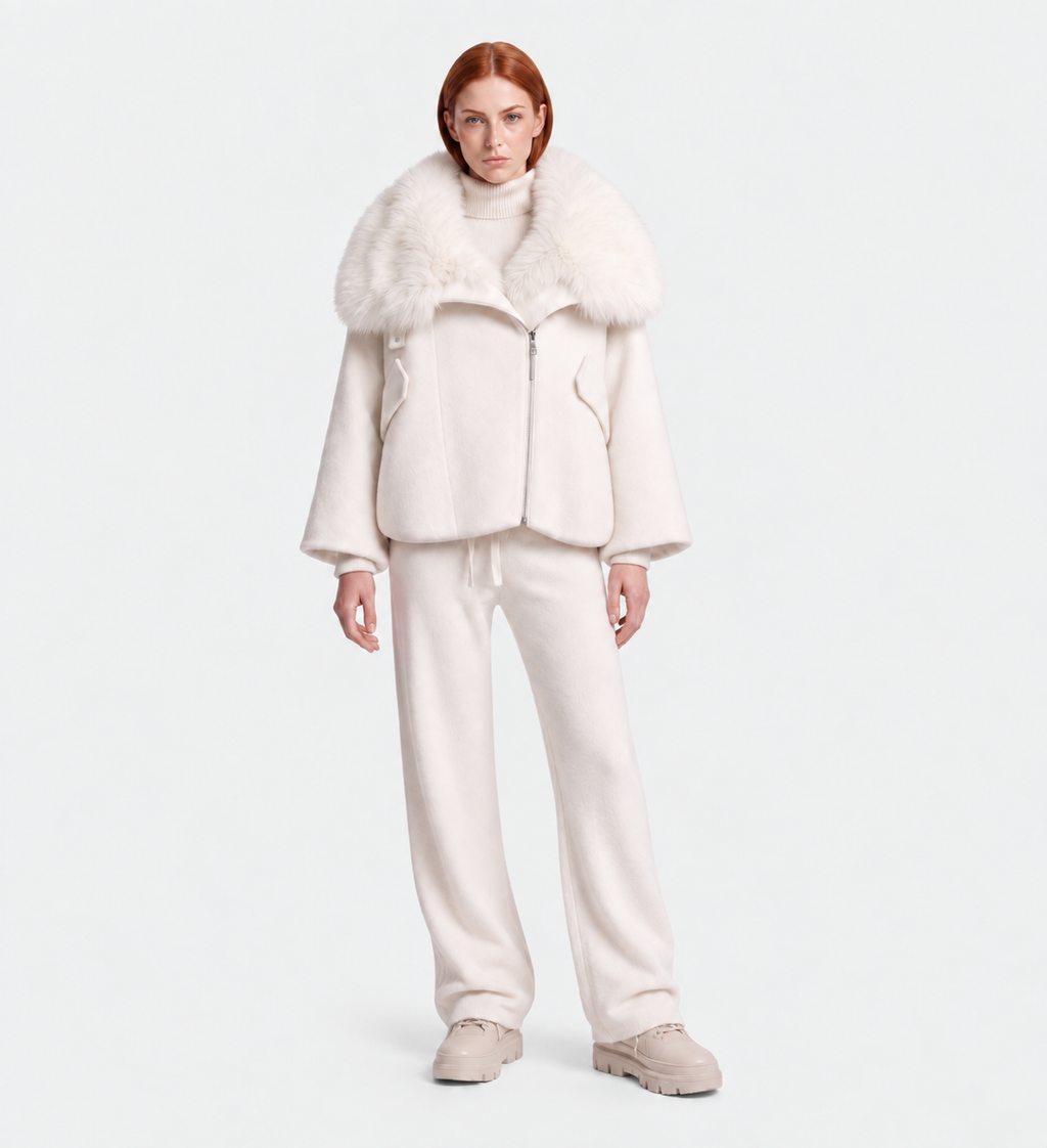 A person with straight red hair wears the ZARIA - 8126999 Vanilla by Rudsak, an all-white winter puffer with faux-fur collar, loose pants, turtleneck, and chunky shoes against a plain light gray background.