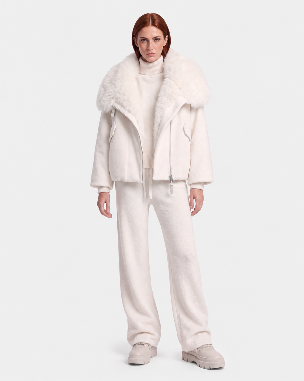 A person with long red hair models the Rudsak ZARIA - 8126999 Vanilla puffer, styled with a white turtleneck, pants, and shoes against a plain white background.