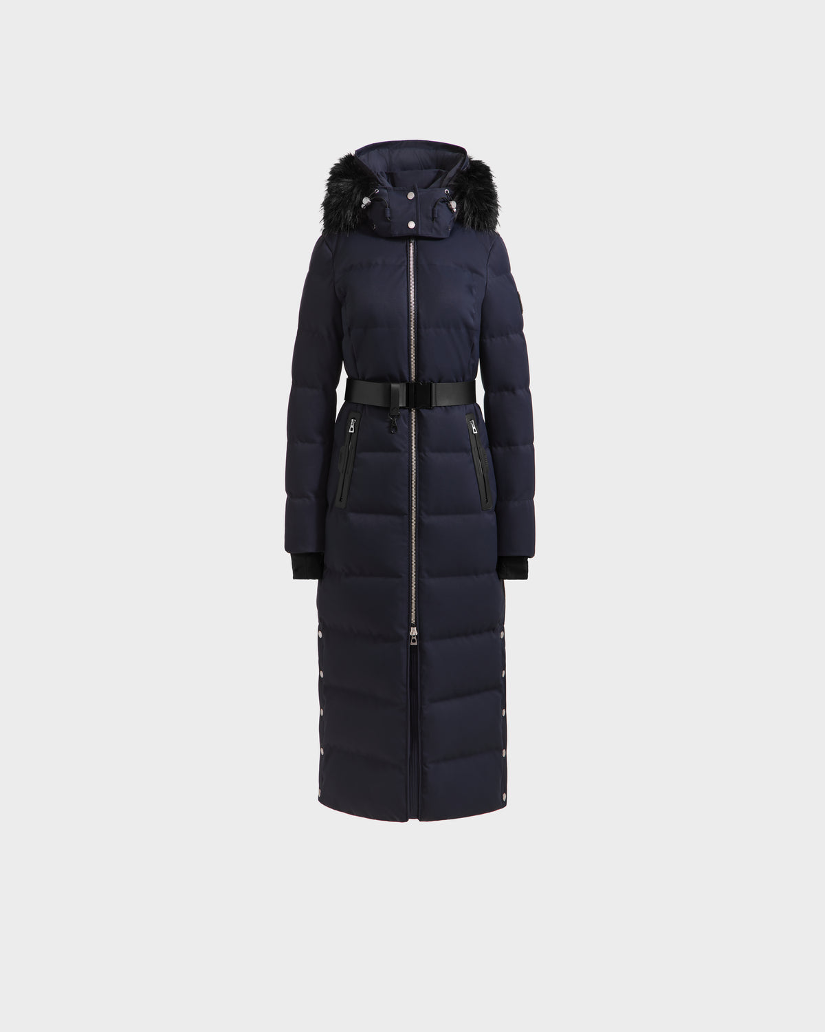 The Rudsak IZABELLA H - 8125644 Navy is a long women’s puffer coat in dark navy, featuring a black fur-trimmed hood, front zipper, black waist belt, zippered side pockets, and snap side buttons. Displayed on a plain white background.
