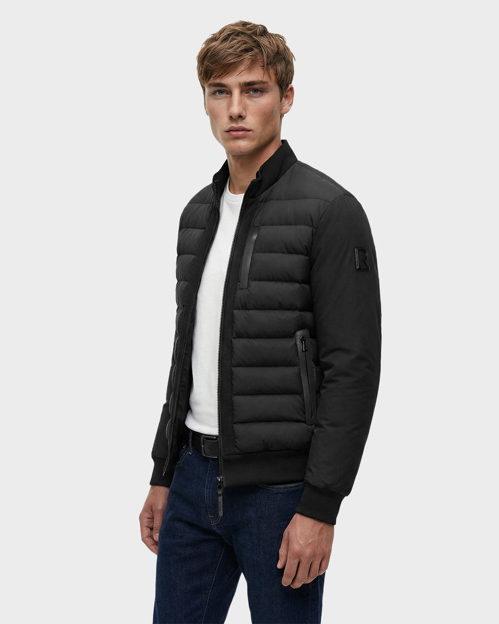 A young man wearing the Rudsak JIMMY - 6125723 Black quilted down jacket over a white t-shirt and dark jeans stands against a plain gray background, looking directly at the camera with a neutral expression.