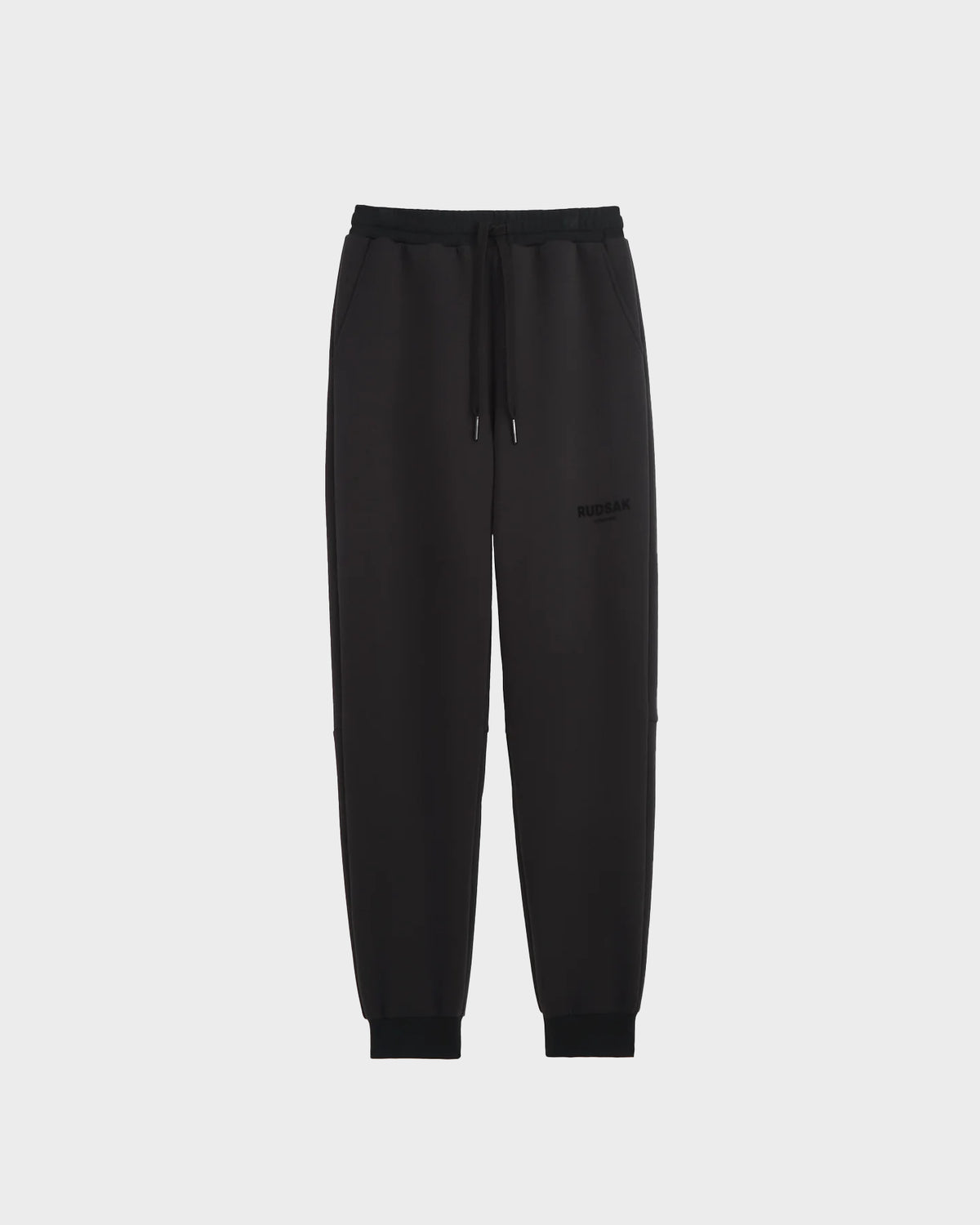 The Rudsak JOSS - 9524009 Black W joggers are made from premium cotton with an elastic waistband, drawstring, side pockets, and ribbed cuffs, shown against a plain light gray background.