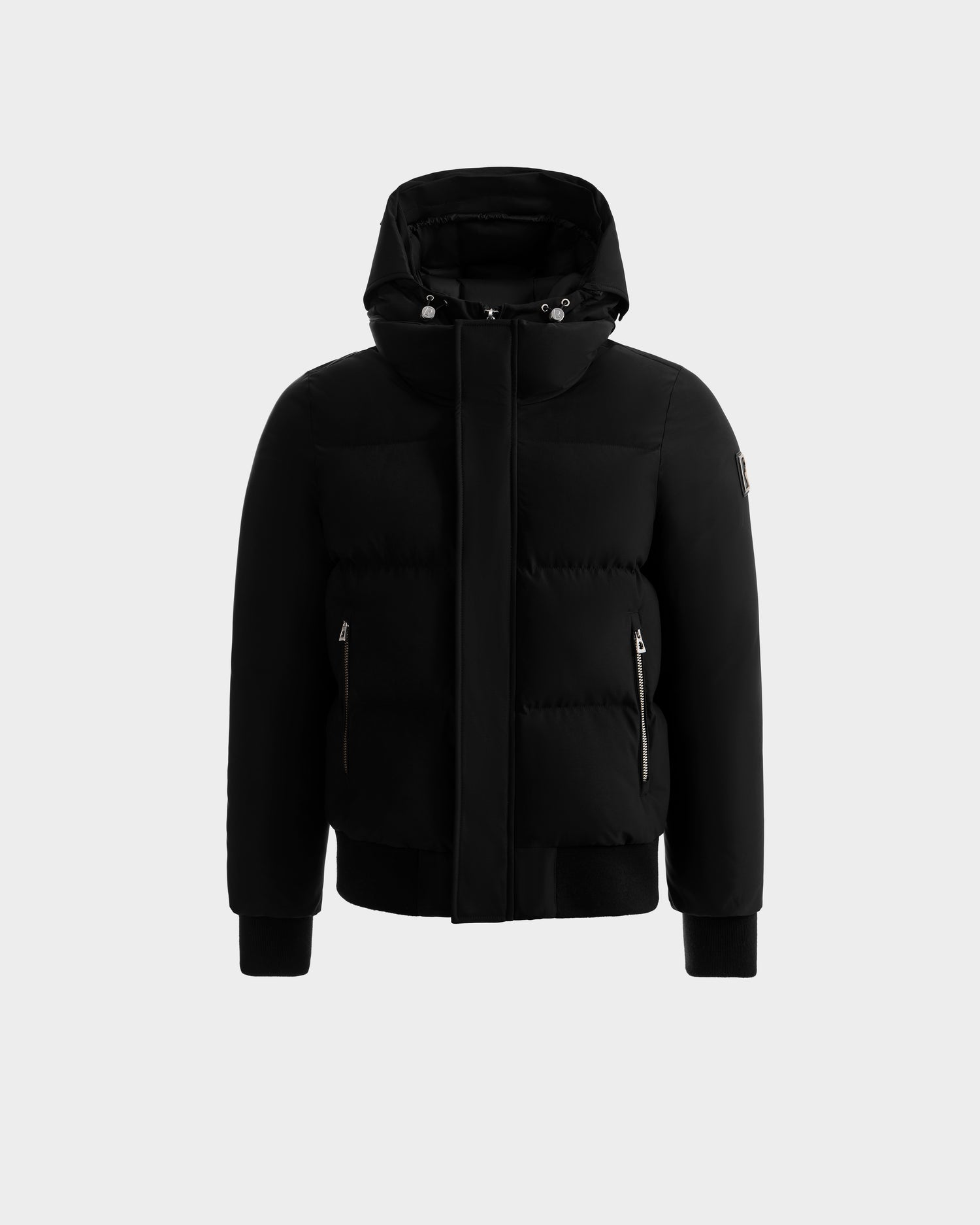 The JORDY - 6125692 Black puffer jacket by Rudsak features a hood, front zipper with flap, two zippered side pockets, ribbed cuffs and hem, displayed on a plain light gray background.