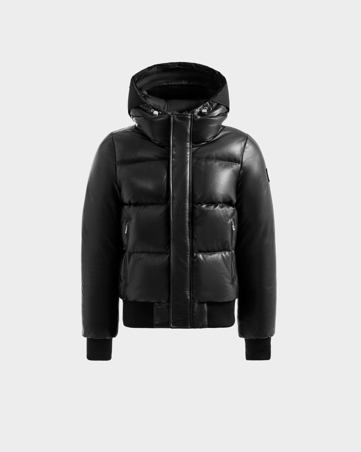 The JORDY X - 6125694 Black by Rudsak is a black quilted bomber jacket with a hood, front zipper, snap buttons, ribbed cuffs, and two zippered side pockets, shown on a plain light gray background.