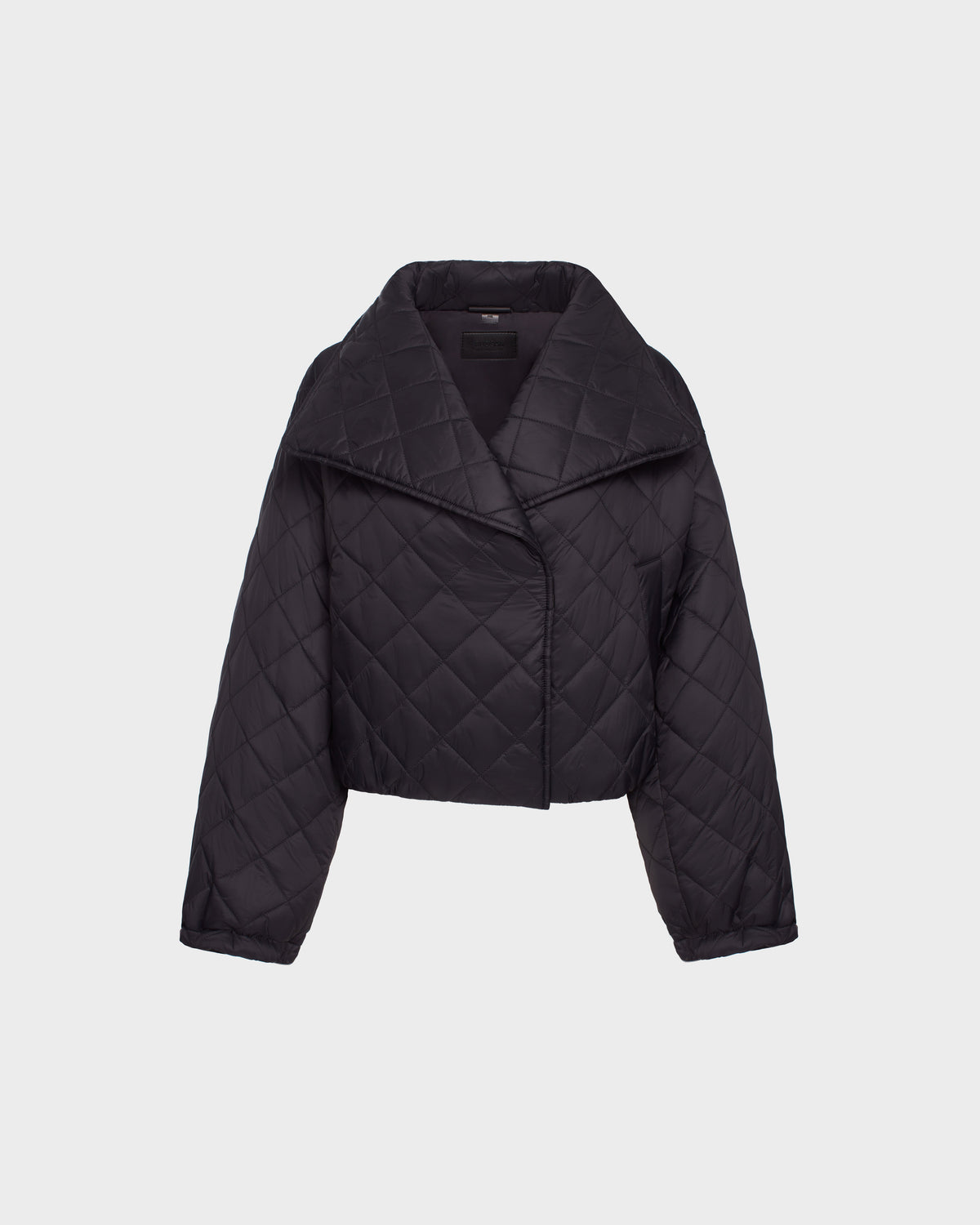 The Rudsak KALEE - 8124005 Black is a womens cropped quilted light jacket with long sleeves, a wide collar, and an asymmetrical front closure, shown against a plain white background.