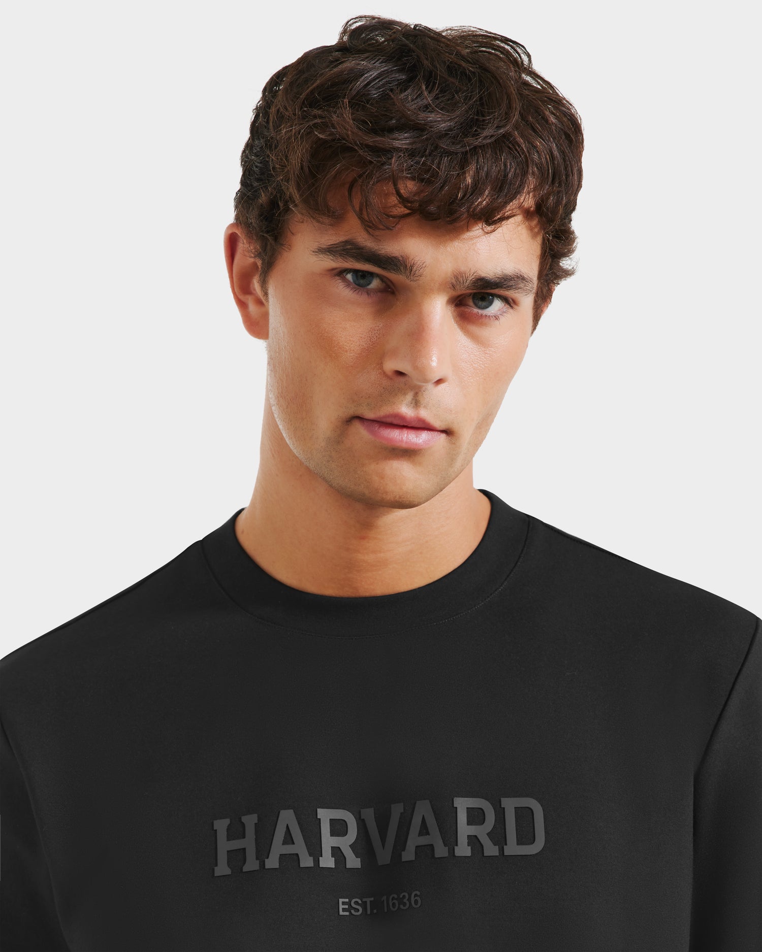 A young man with short, wavy brown hair models the KARTER R HV - H525507 Black by Rudsak as streetwear, standing against a plain white background.