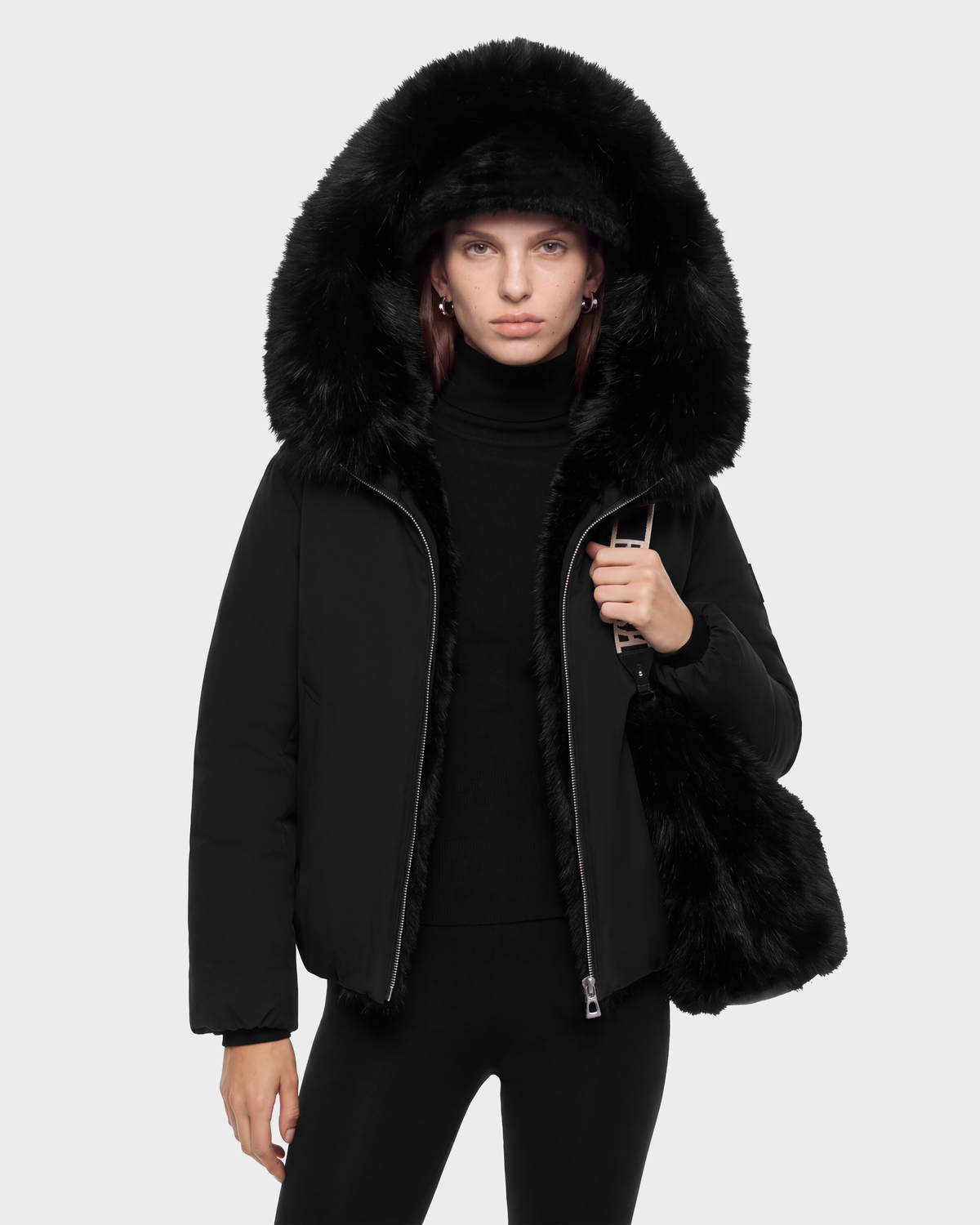 A person wears a black KATHLEEN - 8126764 Black puffer jacket with a large faux fur-trimmed hood and carries a black faux fur bag.