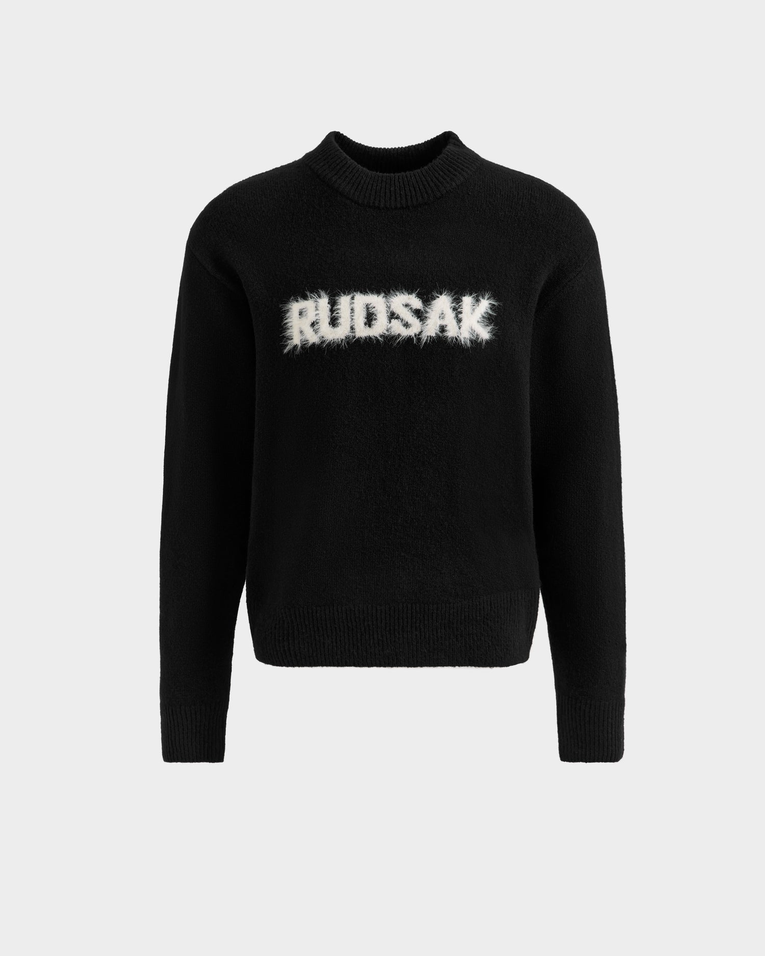 The Rudsak KINLEY - 9525555 Black W is a unisex crewneck sweater with ribbed cuffs and hem, showcasing a large white fuzzy RUDSAK logo on the chest, set against a plain light gray background.