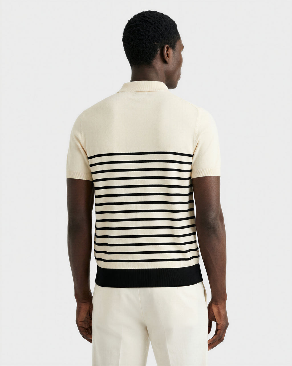A man faces away, wearing the KRIS - 6526005 Iceland men's summer polo by Rudsak with black contrast stripes on the back, paired with matching cream pants, set against a plain light background.