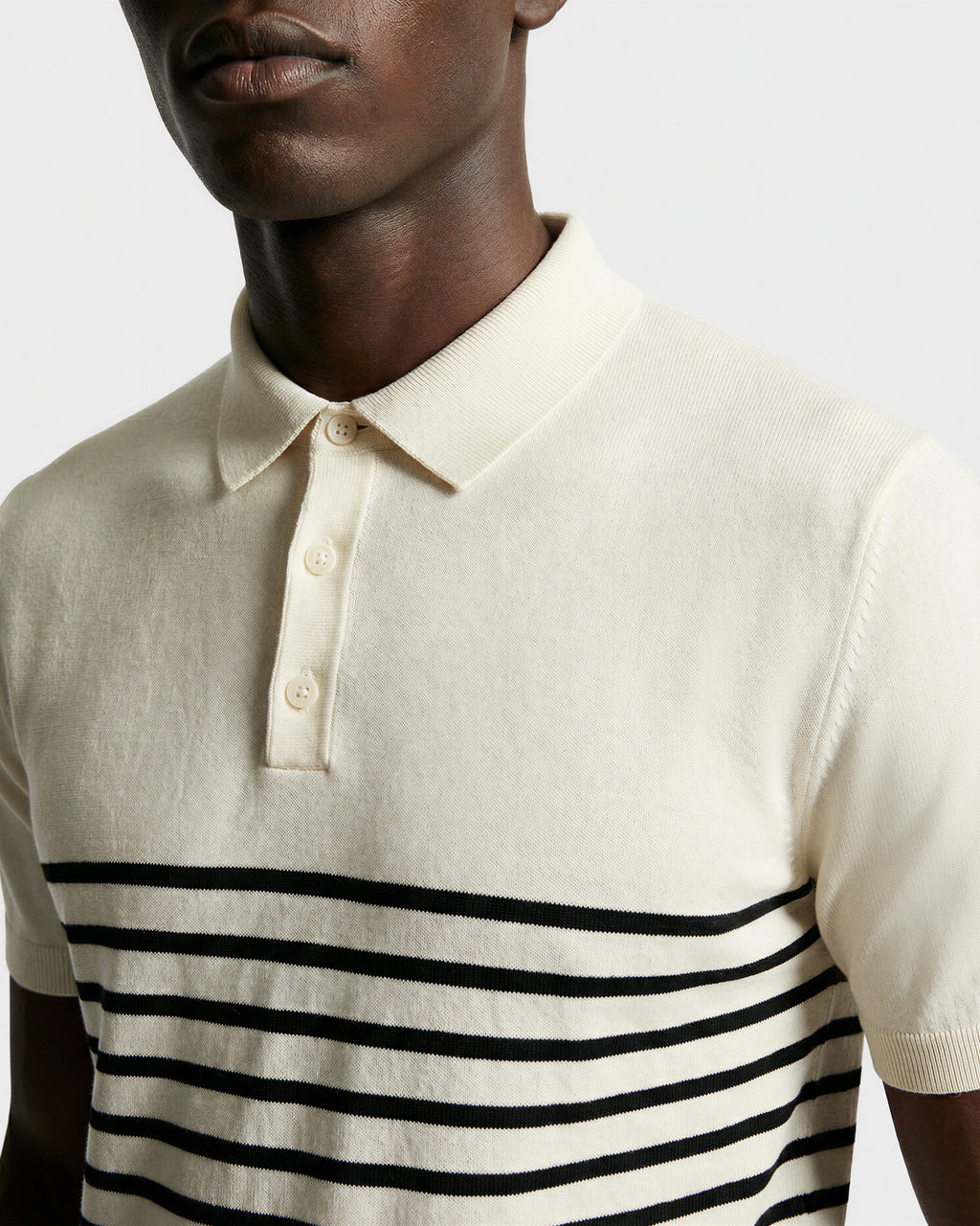 A person wears the KRIS - 6526005 Iceland by Rudsak, a cream fine-gauge knit polo with a collar and black contrast stripes across the chest and sleeves, shown from shoulders to mid-torso against a plain background.