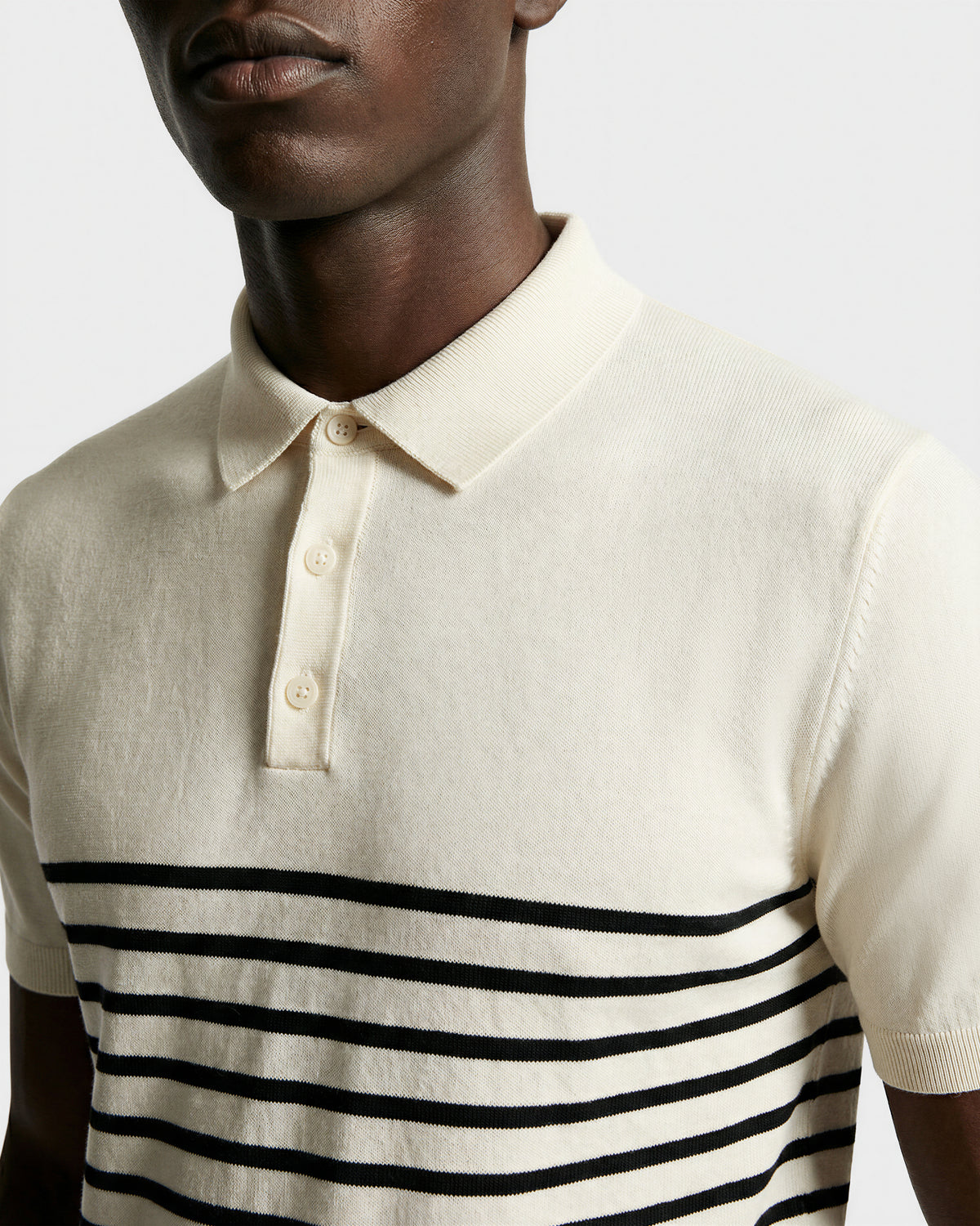 A person wears the KRIS - 6526005 Iceland by Rudsak, a cream fine-gauge knit polo with a collar and black contrast stripes across the chest and sleeves, shown from shoulders to mid-torso against a plain background.
