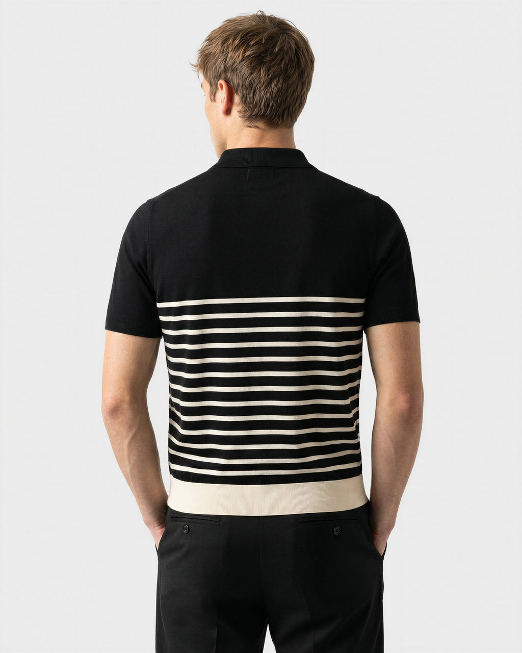 A man faces away, wearing the Rudsak KRIS - 6526005 Black short-sleeve shirt with a contrasting stripe pattern on the lower half and black pants, set against a plain light background.