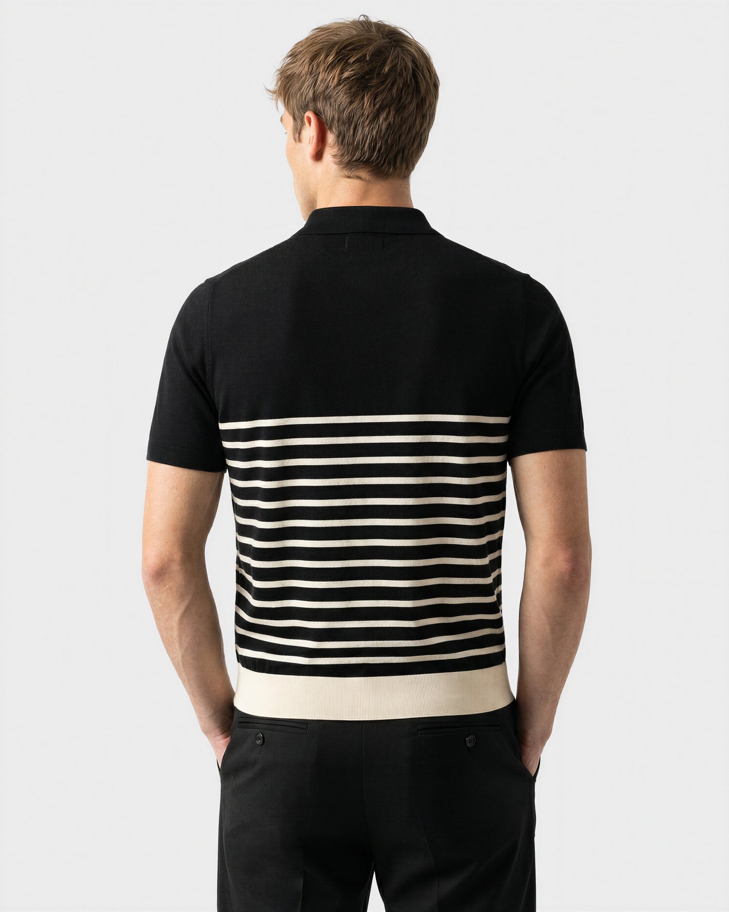 A man faces away, wearing the Rudsak KRIS - 6526005 Black short-sleeve shirt with a contrasting stripe pattern on the lower half and black pants, set against a plain light background.