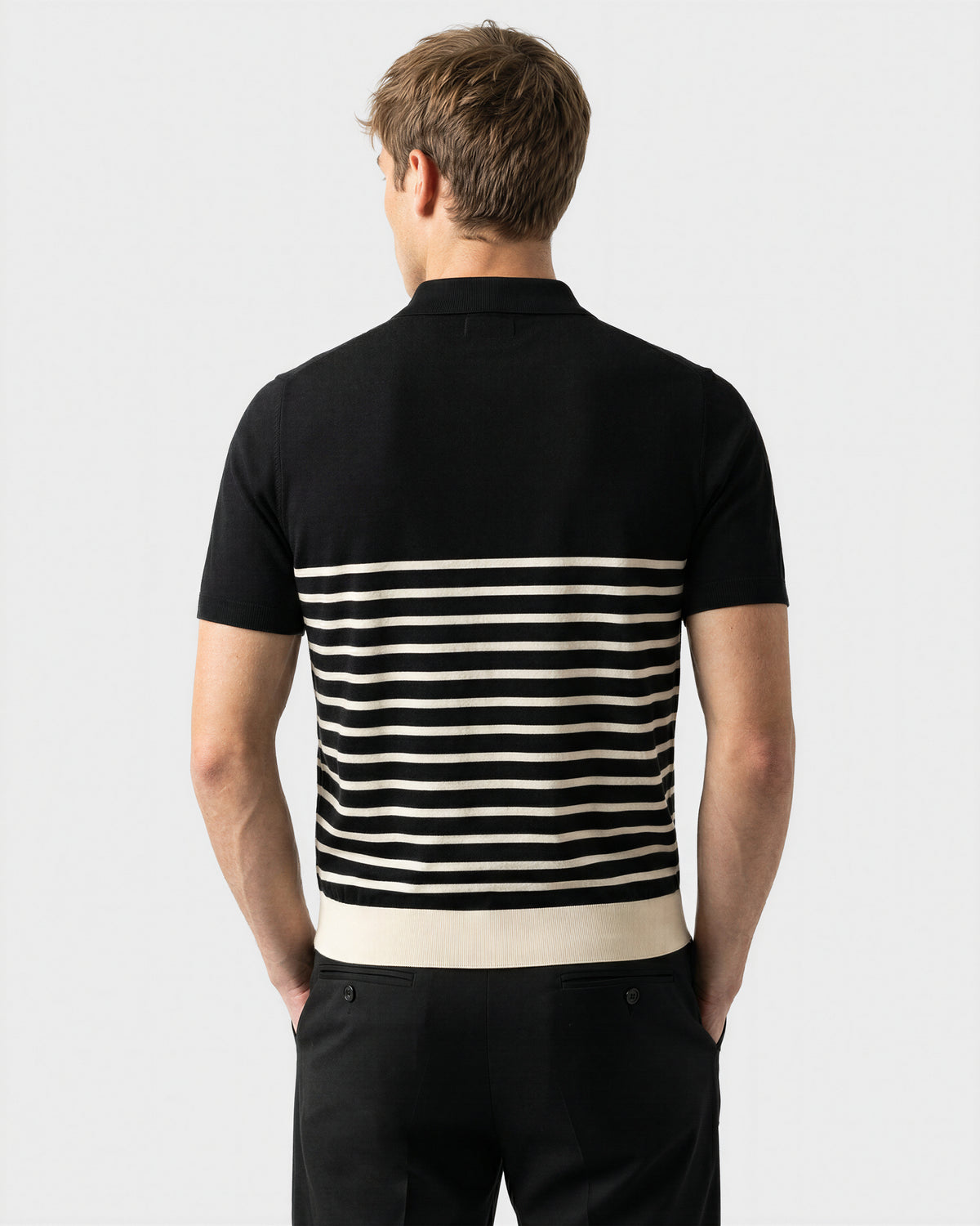 A man faces away, wearing the Rudsak KRIS - 6526005 Black short-sleeve shirt with a contrasting stripe pattern on the lower half and black pants, set against a plain light background.