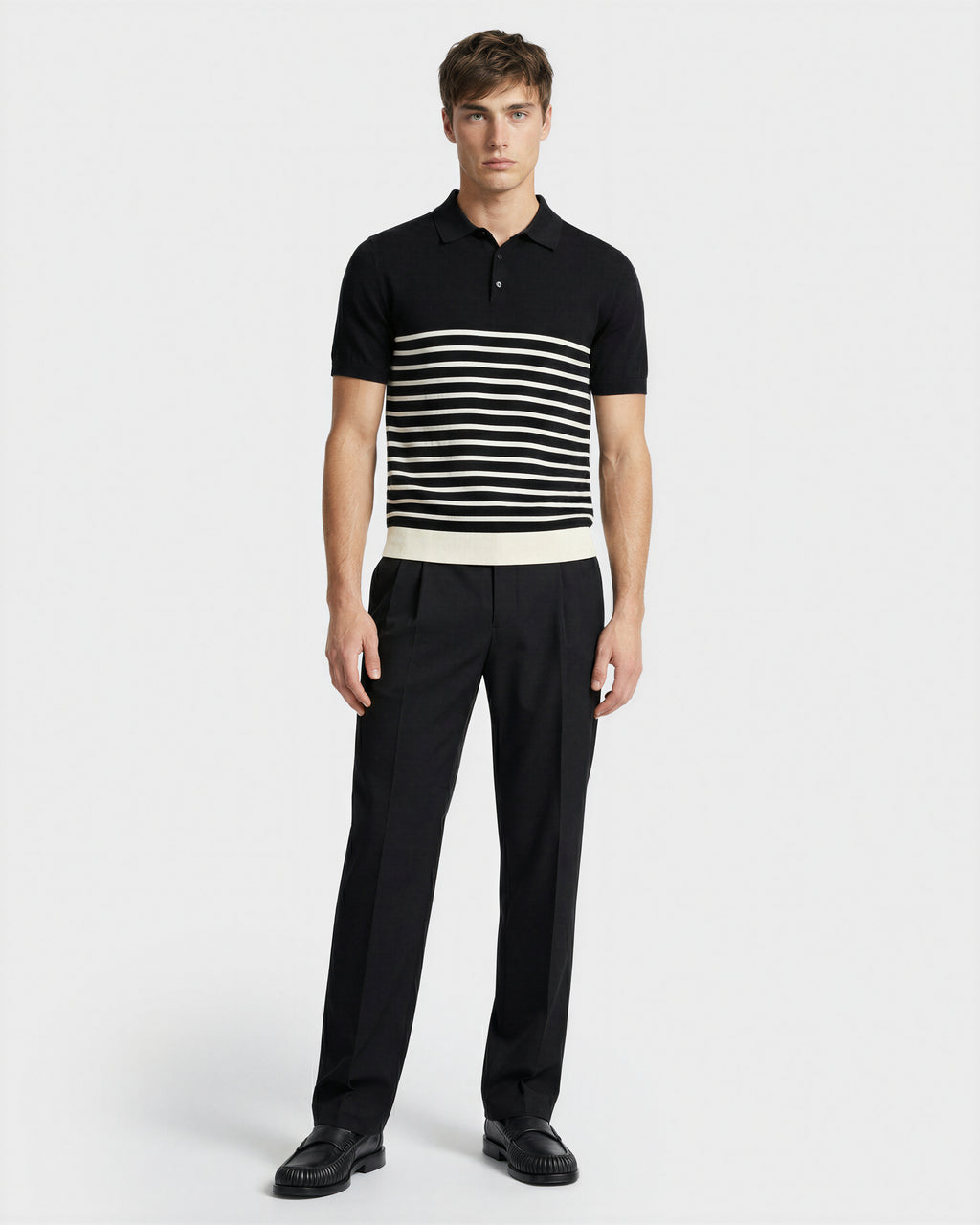 A man faces forward wearing the Rudsak KRIS - 6526005 Black fine-gauge knit polo with bold white chest stripes and black dress pants, set against a plain white background for a sharp, graphic look.