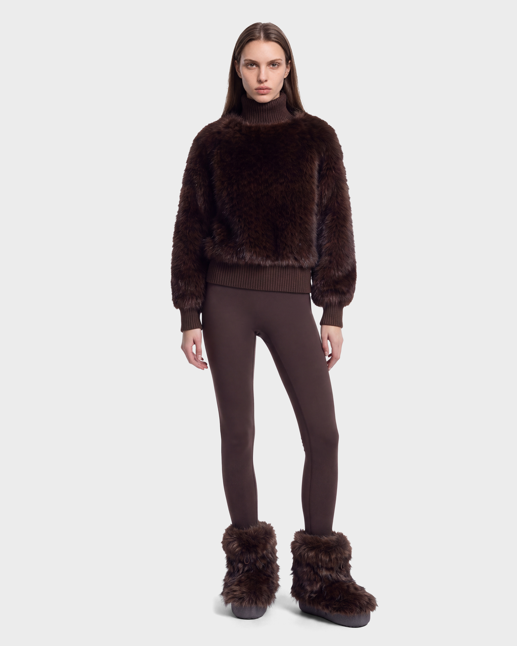 A person wearing a brown cable textured faux fur turtleneck with ribbed trim, brown leggings, and brown faux fur-trimmed boots in an après-ski style featuring the Rudsak LAYLA F - 8525630 Mix Expresso.