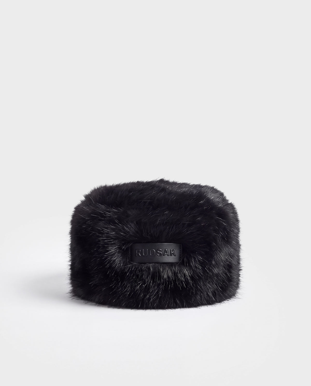 Black faux fur LORETTA - 8426503 Black pillbox hat with a centered rectangular leather patch embossed with the Rudsak brand name.
