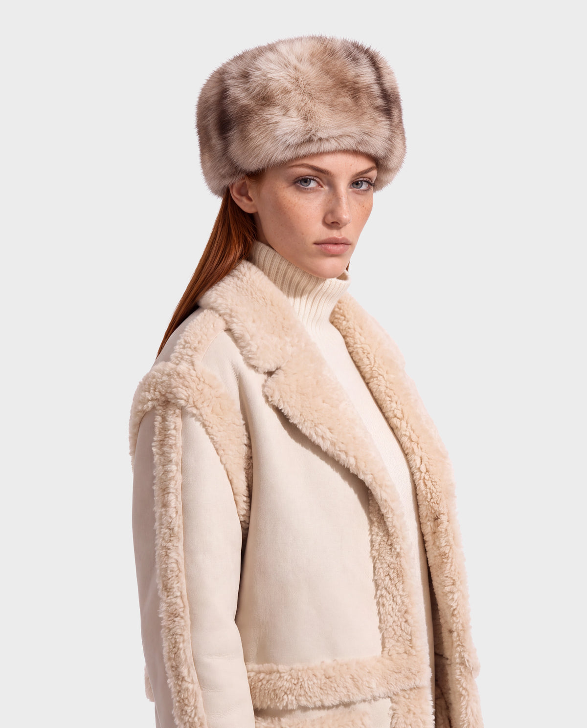 A person wearing a LORETTA - 8426503 Mix Vanilla shearling-lined coat over a turtleneck sweater and a matching fur-textured hat.