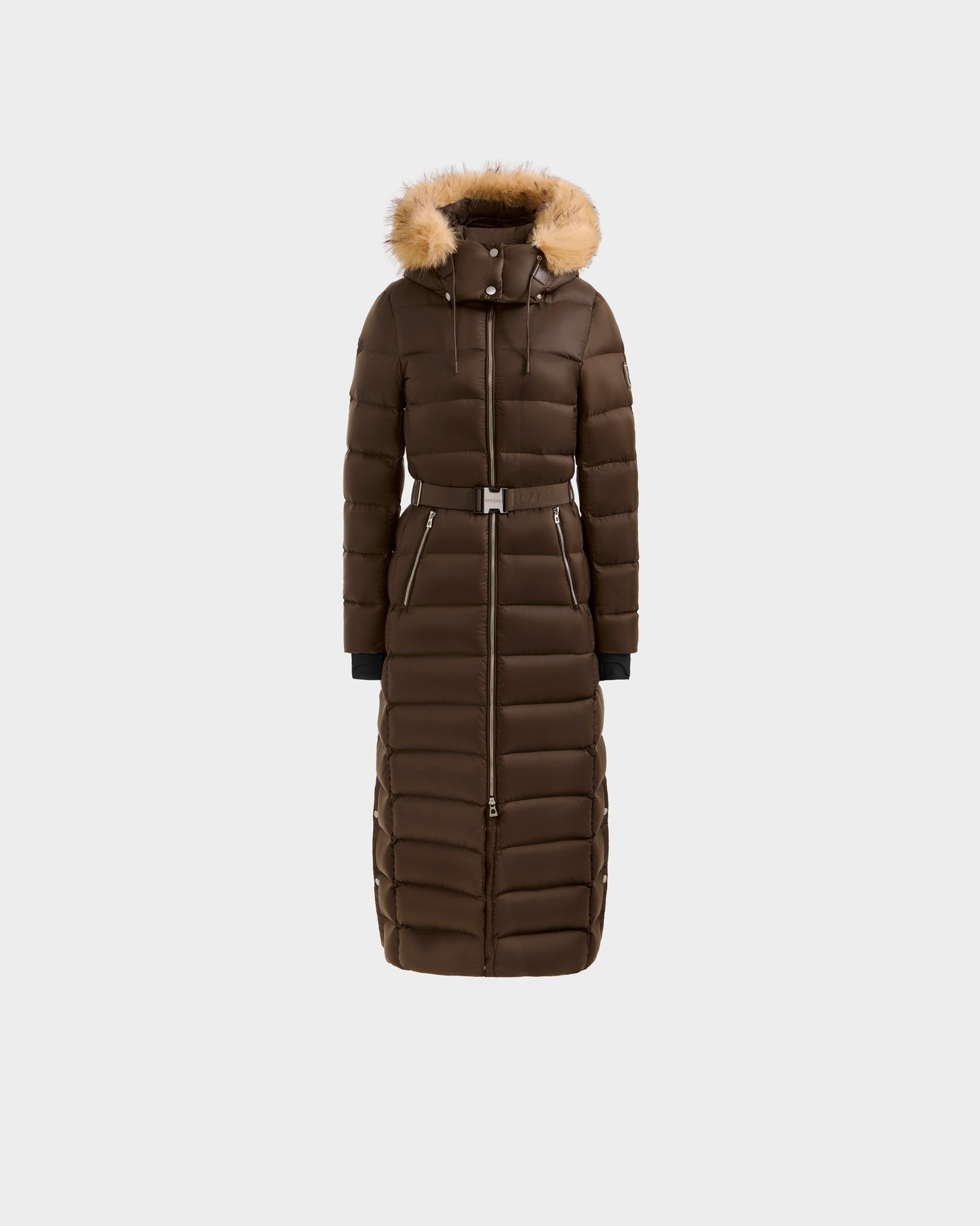 The Rudsak LILITH L - L125528 Espresso is a maxi-length down puffer coat with a belted waist, black cuffs, vertical and horizontal stitching, and a hood trimmed with light brown faux fur, shown on a plain white background.