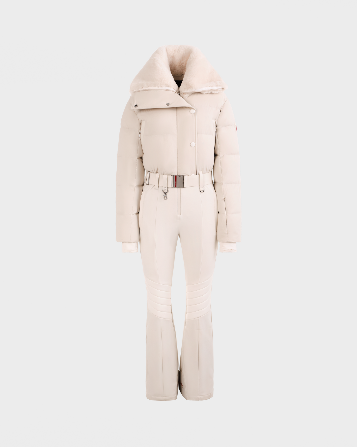 The Rudsak LOVE - 8124724 Vanilla is a stylish off-white women’s one-piece ski suit with a belted waist, flared pants, high collar, and faux fur-trimmed jacket, displayed on a plain light gray background.