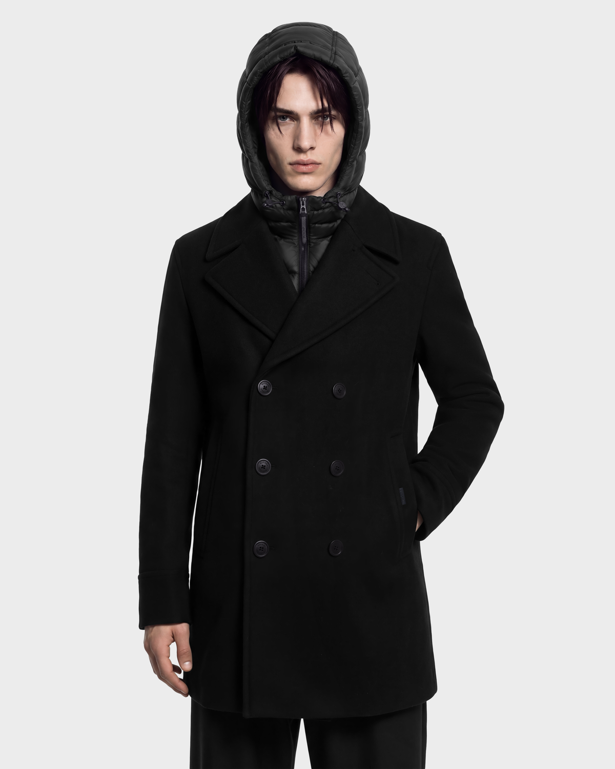 A person wearing a black Rudsak LUCIEN - 6126508 Black double-breasted pea coat over a hooded quilted jacket.