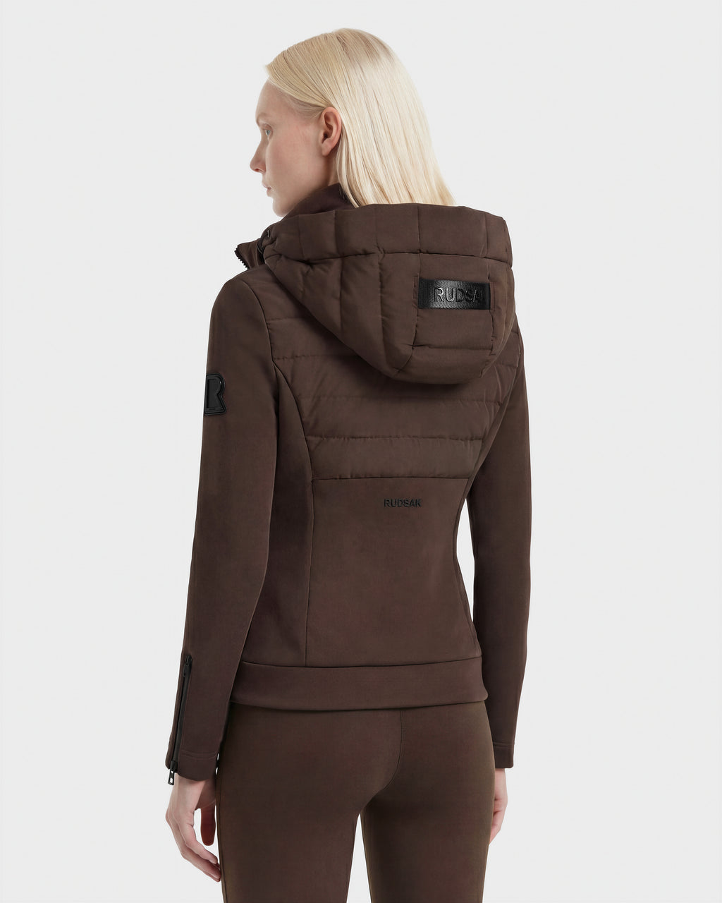 A person with straight, light blonde hair is modeling the Rudsak MABS - 8124825 Espresso dark brown detachable hood jacket and matching pants, standing with their back to the camera against a plain white background.