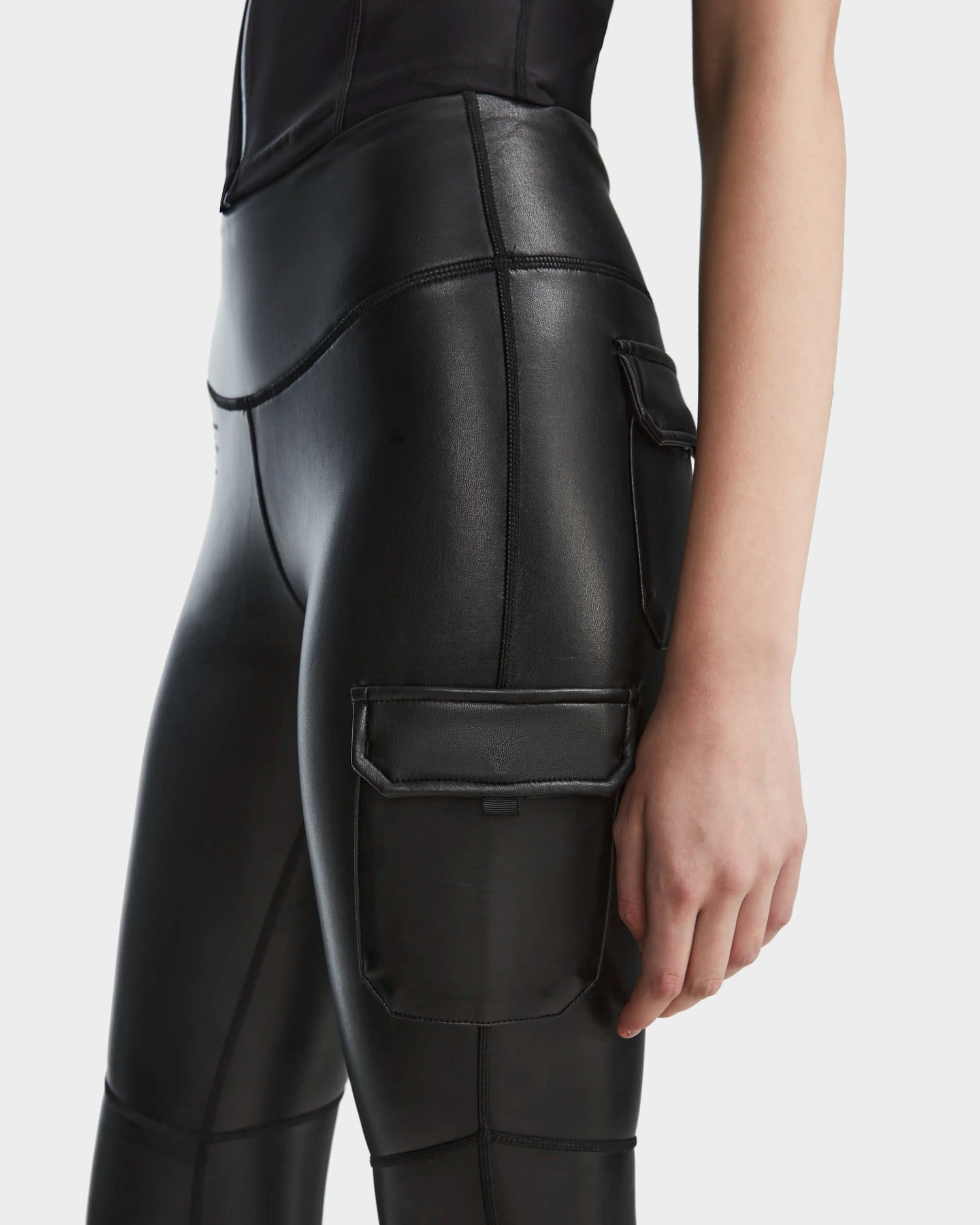 A person is shown from the waist to mid-thigh wearing Rudsak's SIEN L - 8524079 high-waisted black vegan leather leggings with cargo pockets against a plain background.