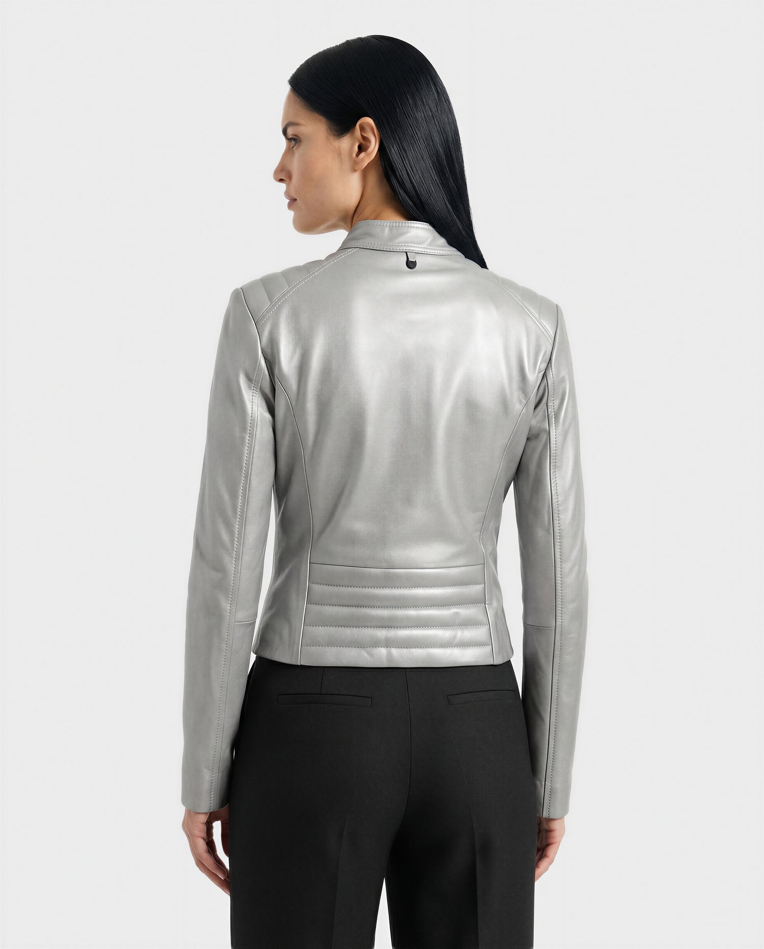 A woman with long dark hair, seen from the back, wears the Rudsak MERINA - L120013 Metallic Aluminium jacket with black pants against a plain light gray background.