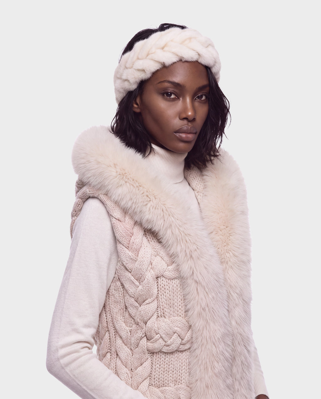 A woman wears the Rudsak MILA - 8426518 Vanilla cream-colored chunky knit vest with a faux fur collar and a matching braided faux fur headband.