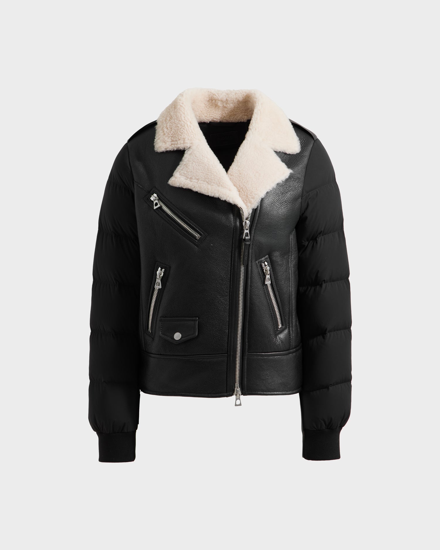 The Rudsak MALA - 8125628 Black women’s shearling jacket features puffy quilted sleeves, a cropped fit, silver zippers, a flap pocket with snap button, and a wide cream shearling collar, shown on a white background.