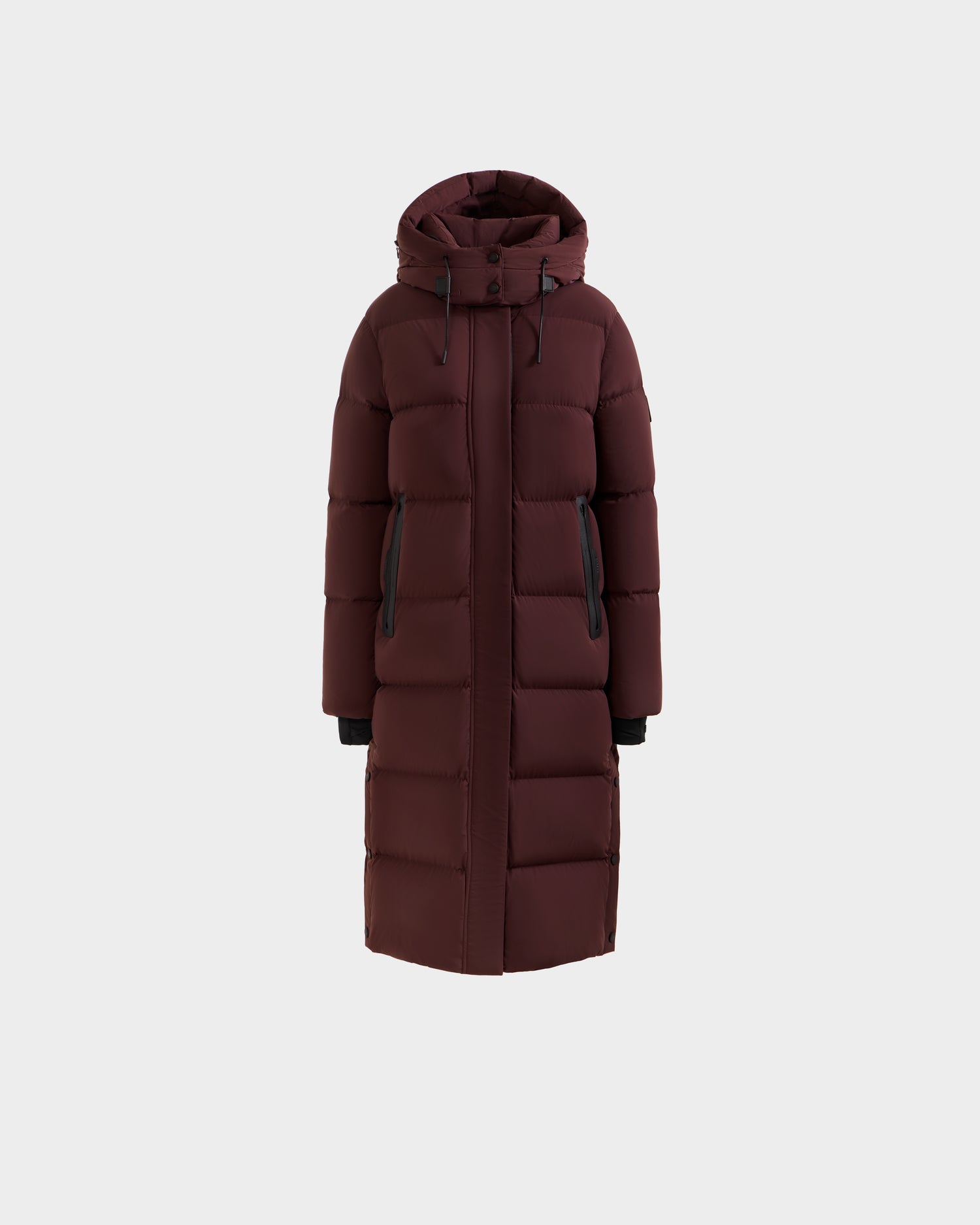 Rudsak MAO - 8124780 Bordeaux women’s long down coat in maroon features a hood, front zipper closure, black zip pockets, and horizontal quilted stitching. Water-resistant and perfect for winter, shown on a plain white background.