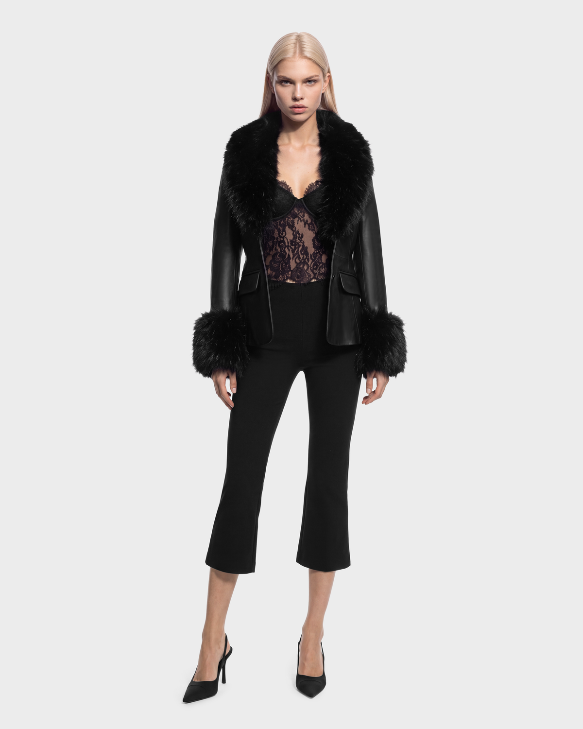 A person wearing a MARILLA - 8126972 Black leather jacket with a black fur collar and cuffs, over a black lace bodysuit and cropped black trousers, paired with black high-heeled pumps.