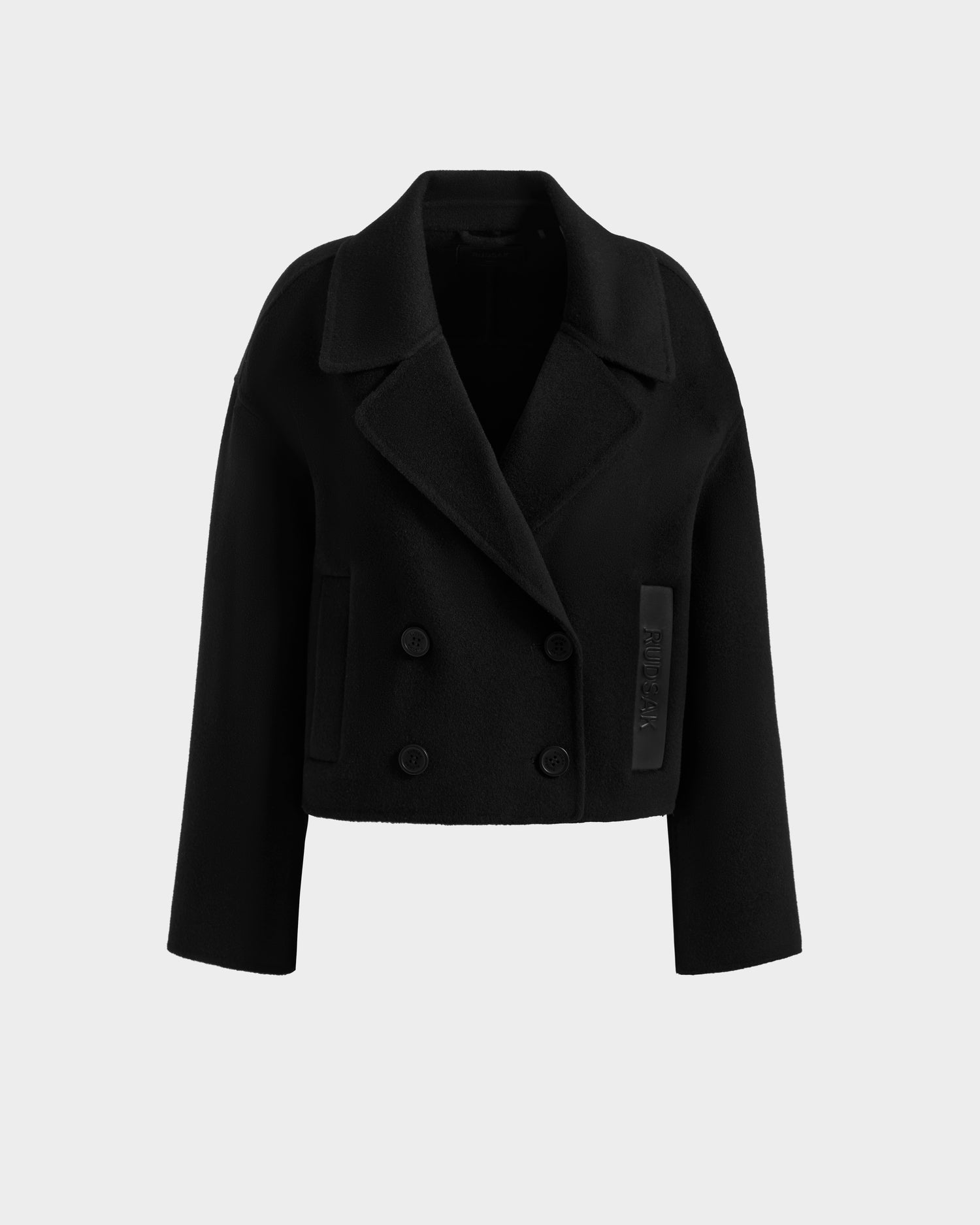 The MARTINEZ - 8125580 Black by Rudsak is a cropped women’s wool-blend coat with wide lapels, long sleeves, front buttons, a stitched patch detail, and double-breasted design, shown on a plain light gray background.